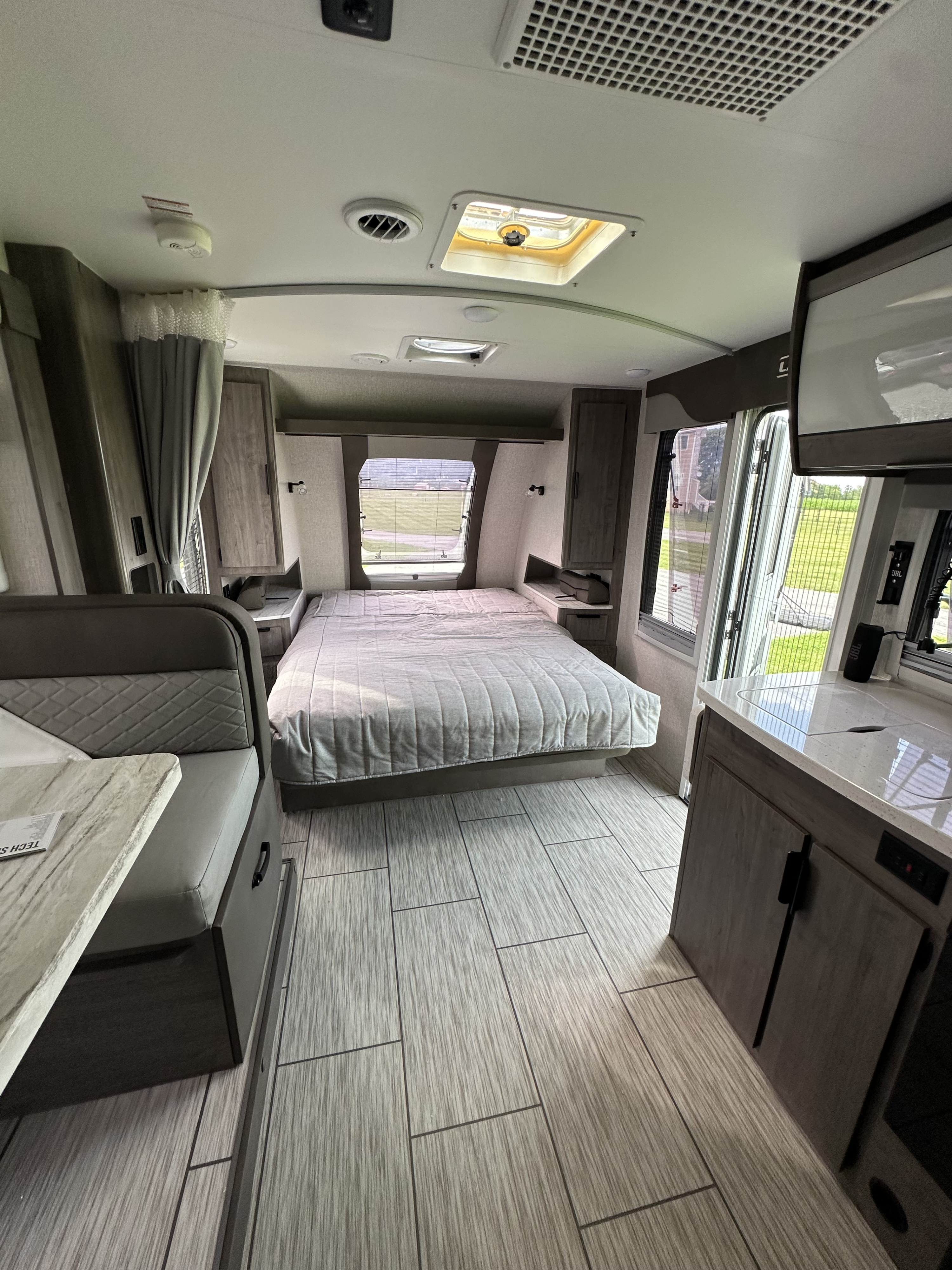 This rv rental features a cozy bed, dining booth, and kitchen counter, with light wood-look tiled flooring and outdoor views.. Lance 2185 2024