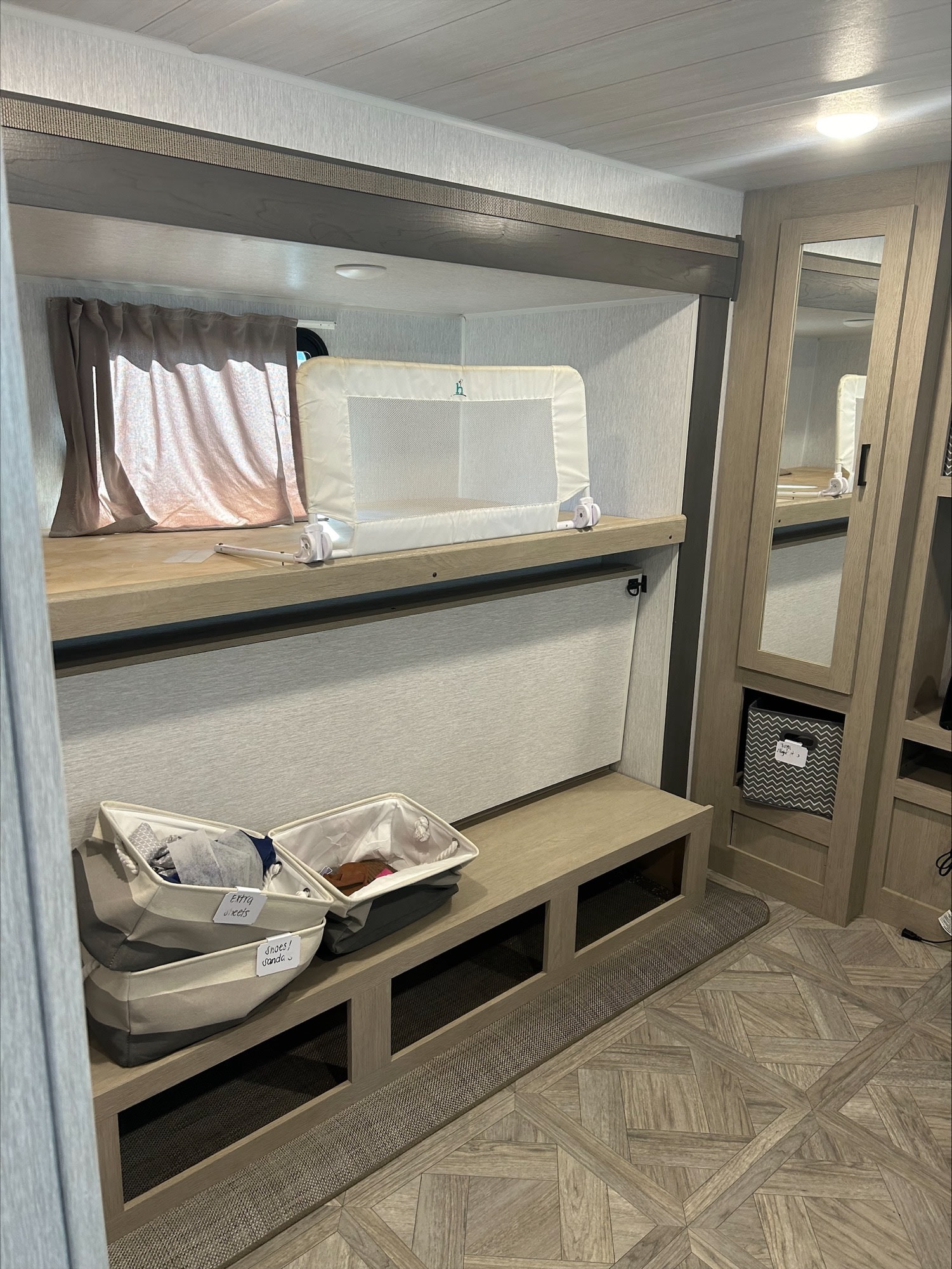 Cozy RV rental bunk bed with baby safety rail, storage bins, and patterned floor. Ideal family space for comfortable travel.. Forest River Wildwood 2024
