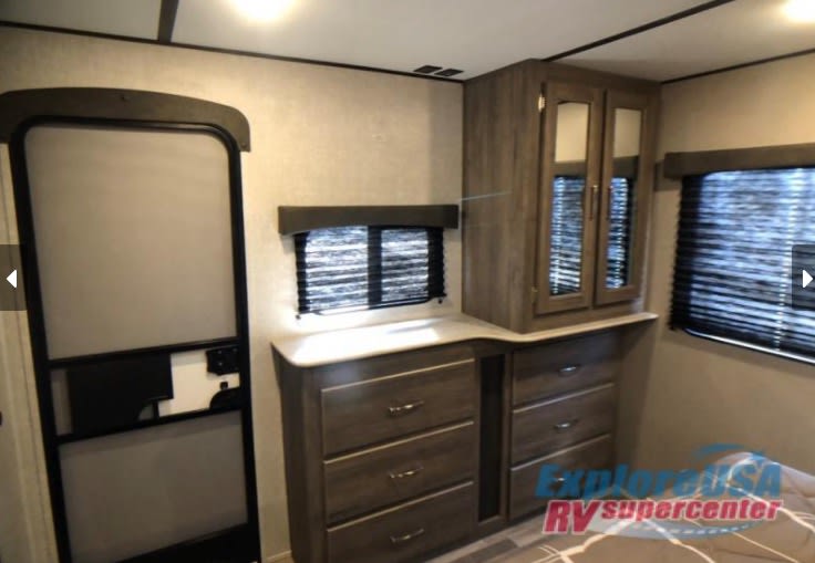 This rv rental bedroom offers practical storage with built-in drawers, a cabinet, windows, and an interior door.. Keystone RV Zinger 2021