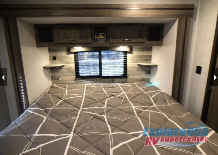 Comfortable RV rental bedroom with a large bed, headboard, window, overhead cabinets, and side shelves.. Keystone RV Zinger 2021