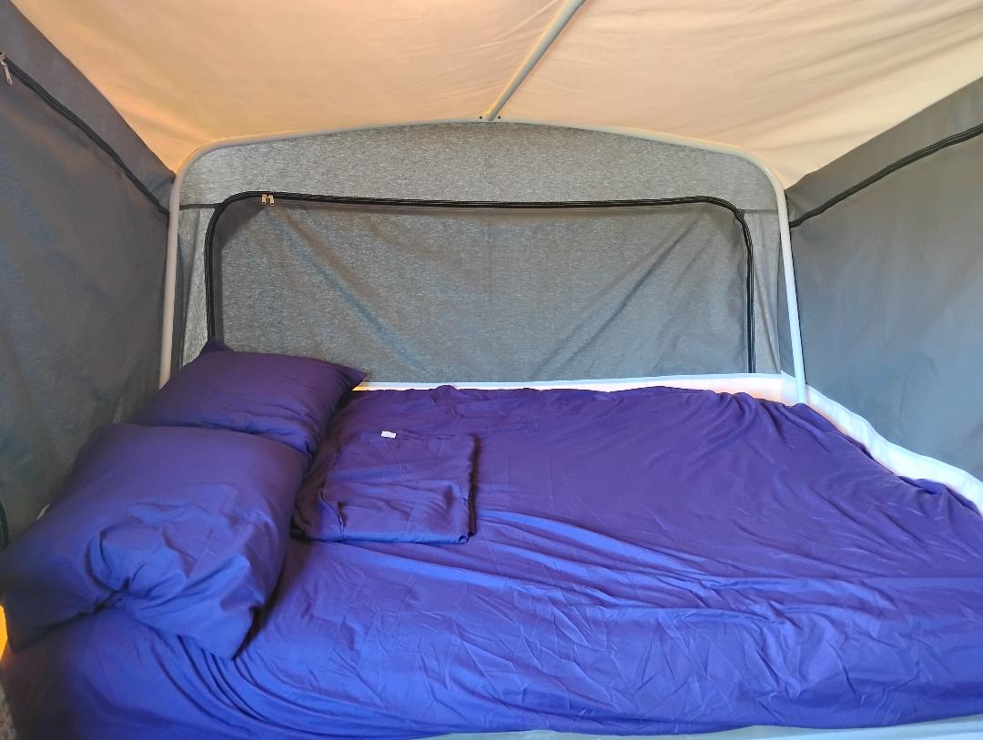 Cozy RV rental pop-up camper bed with vibrant purple sheets and pillows, ready for comfortable sleeping.. Coleman Destiny Taos 1999