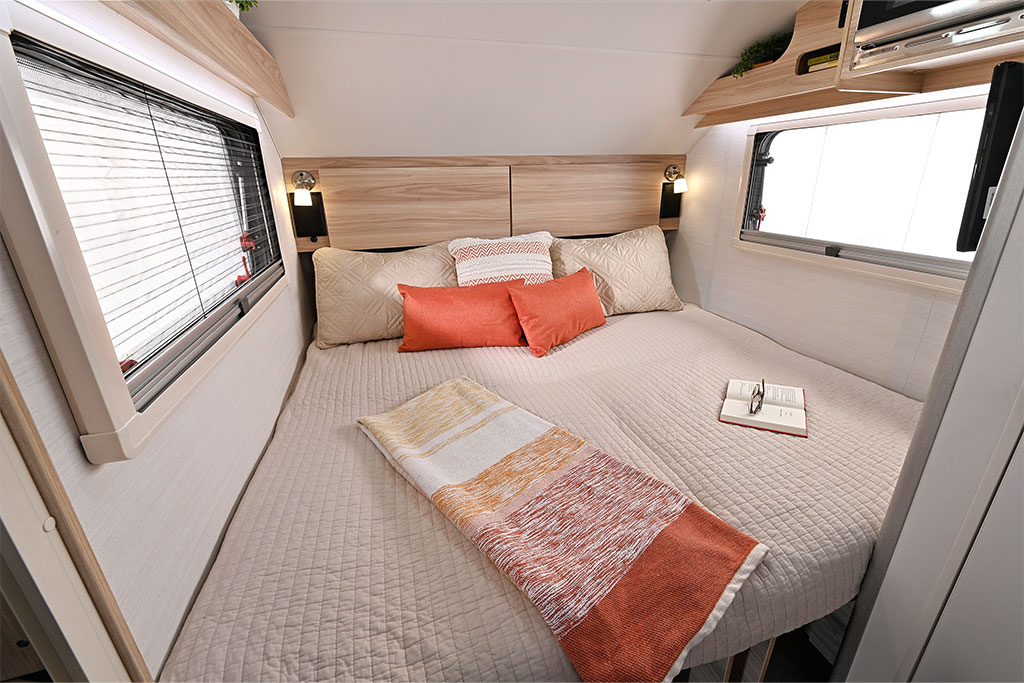 Cozy RV rental bedroom featuring a comfortable bed, windows, reading lamps, and overhead storage shelves.. NuCamp Tab 320 Tear Drop 2025