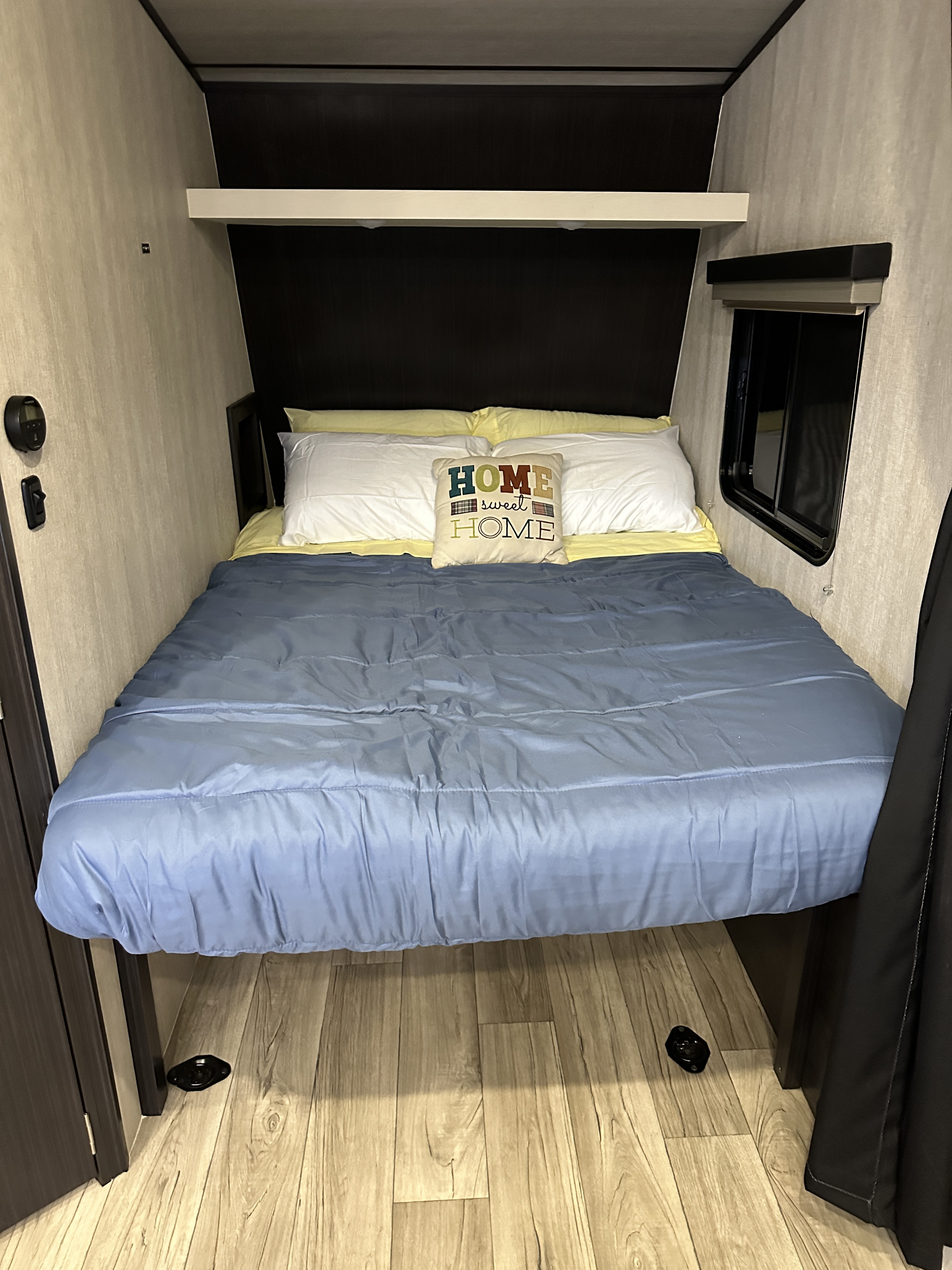 Cozy RV rental bedroom featuring a blue bed, "HOME sweet HOME" pillow, light wood floor, and climate controls.. Genesis Supreme Rv Genesis Supreme 2025