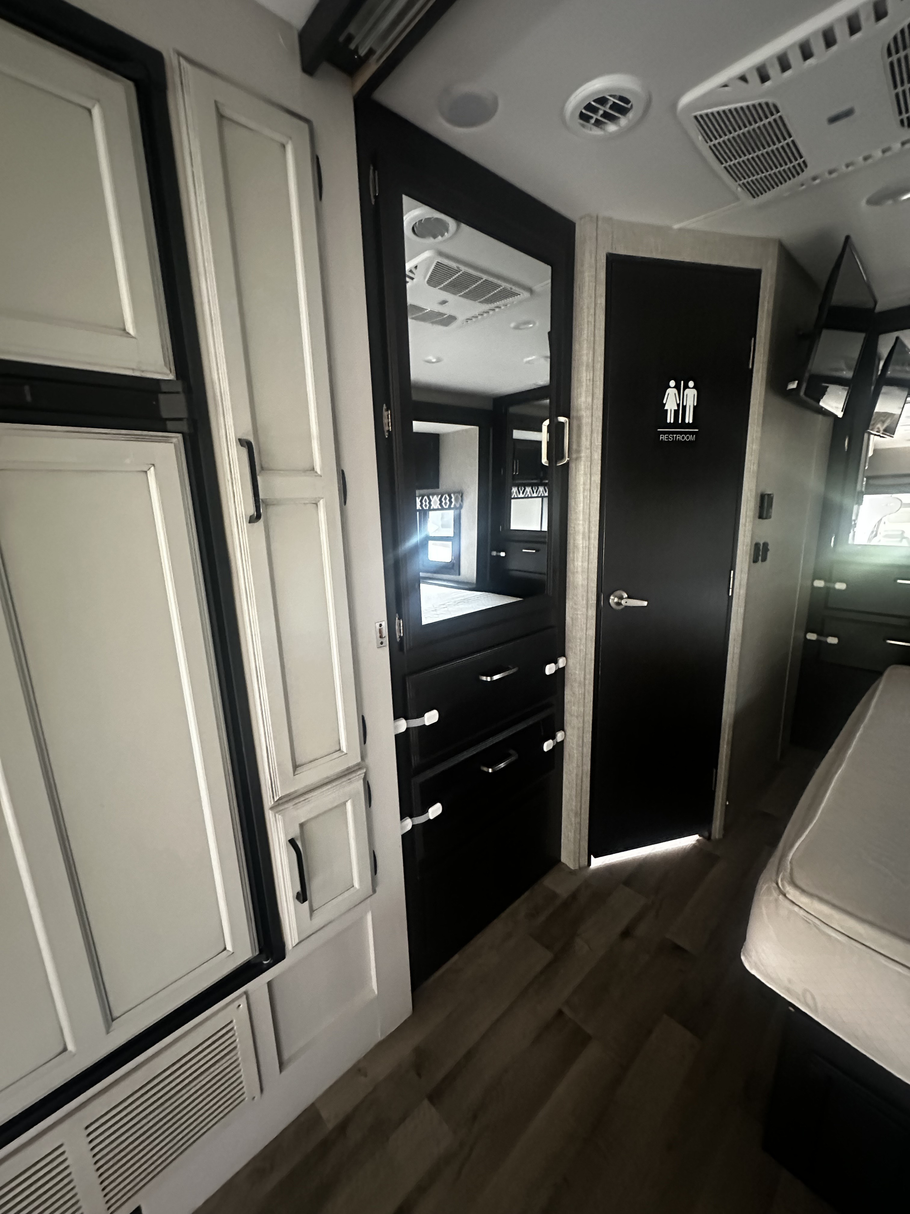 Inside an rv rental: restroom door, mirrored wardrobe, and bedroom visible. Light & dark cabinetry, child-safe drawers.. Jayco Greyhawk 2022