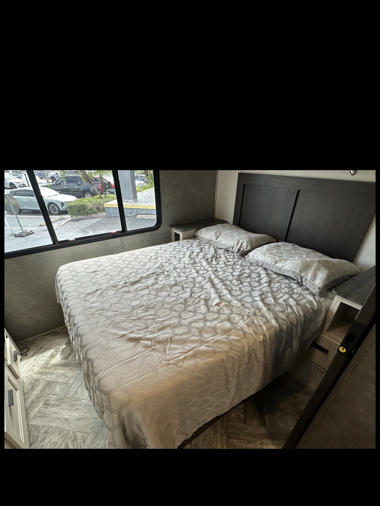 RV rental bedroom: Comfortable bed with patterned comforter, dark headboard, and outdoor window view.. Forest River Sunseeker LE 2024
