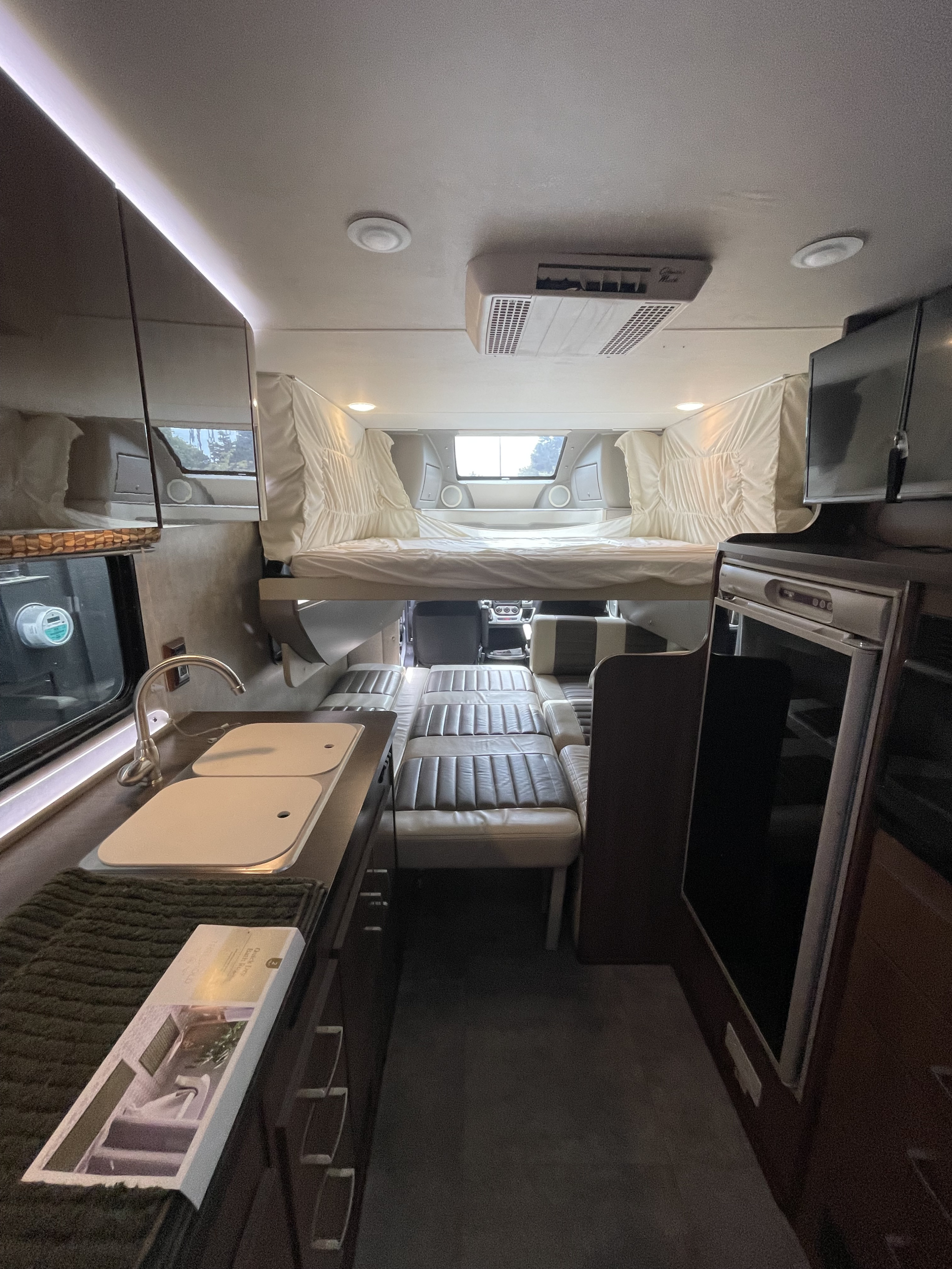 Inside this rv rental: overhead bed, kitchen sink, and convertible seating area. Compact and functional travel space.. Winnebago Trend 2015