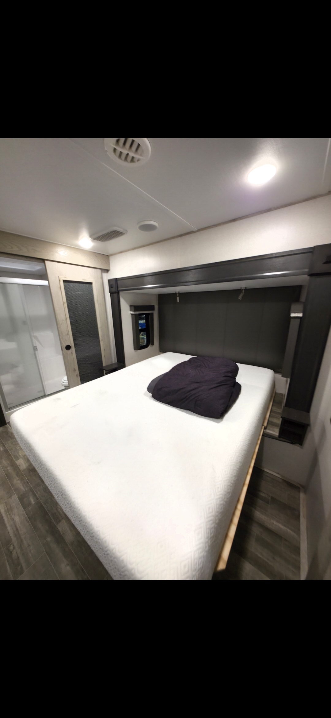RV rental: A compact bedroom with a white mattress, dark blanket, built-in storage, and an adjacent shower stall. Ideal for travel.. Keystone RV Alpine 2022
