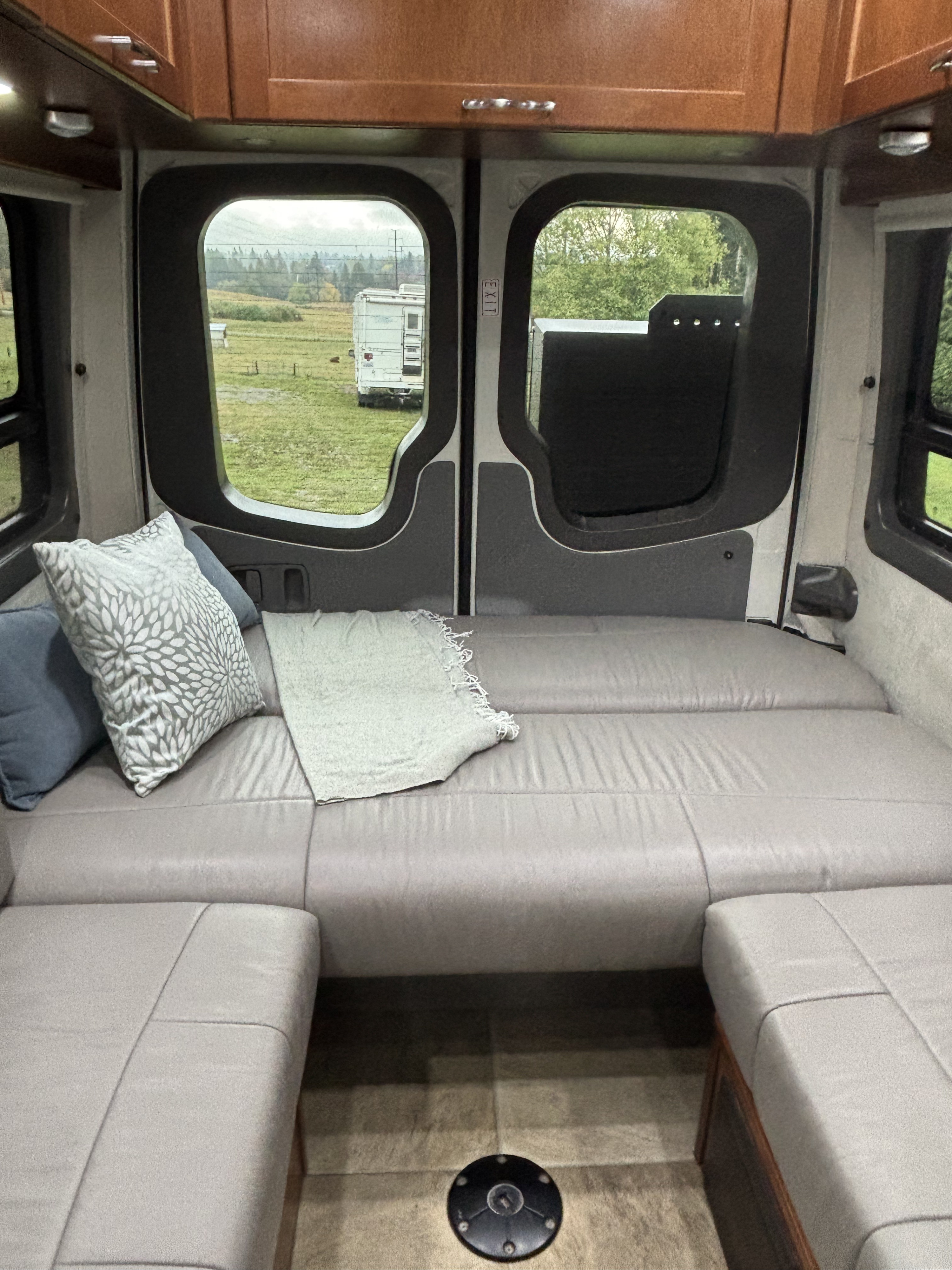 Cozy RV rental interior: rear seating/bed with pillows & blanket, wooden cabinets, and a field view from the back.. Pleasure-Way Pleasure-Way Class B 2016