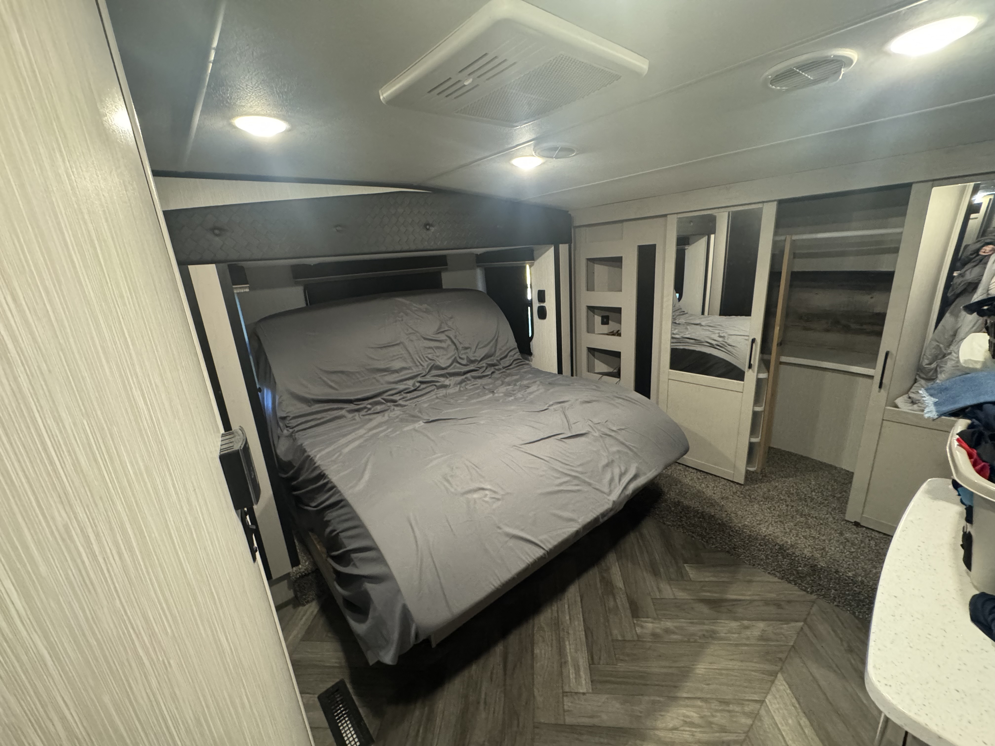 Modern RV rental bedroom with a grey bed, mirrored wardrobes, and stylish herringbone and carpet flooring. Brightly lit.. Heartland Cyclone 2021