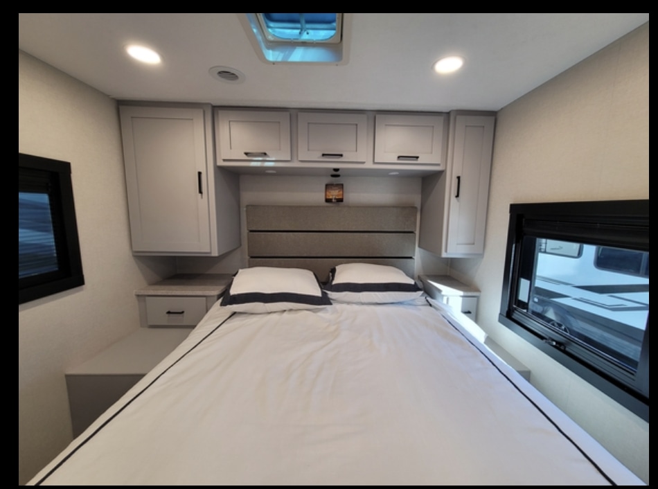 Bright RV rental bedroom features a comfy bed, light grey storage cabinets, and windows.. Coachmen Pursuit 2025