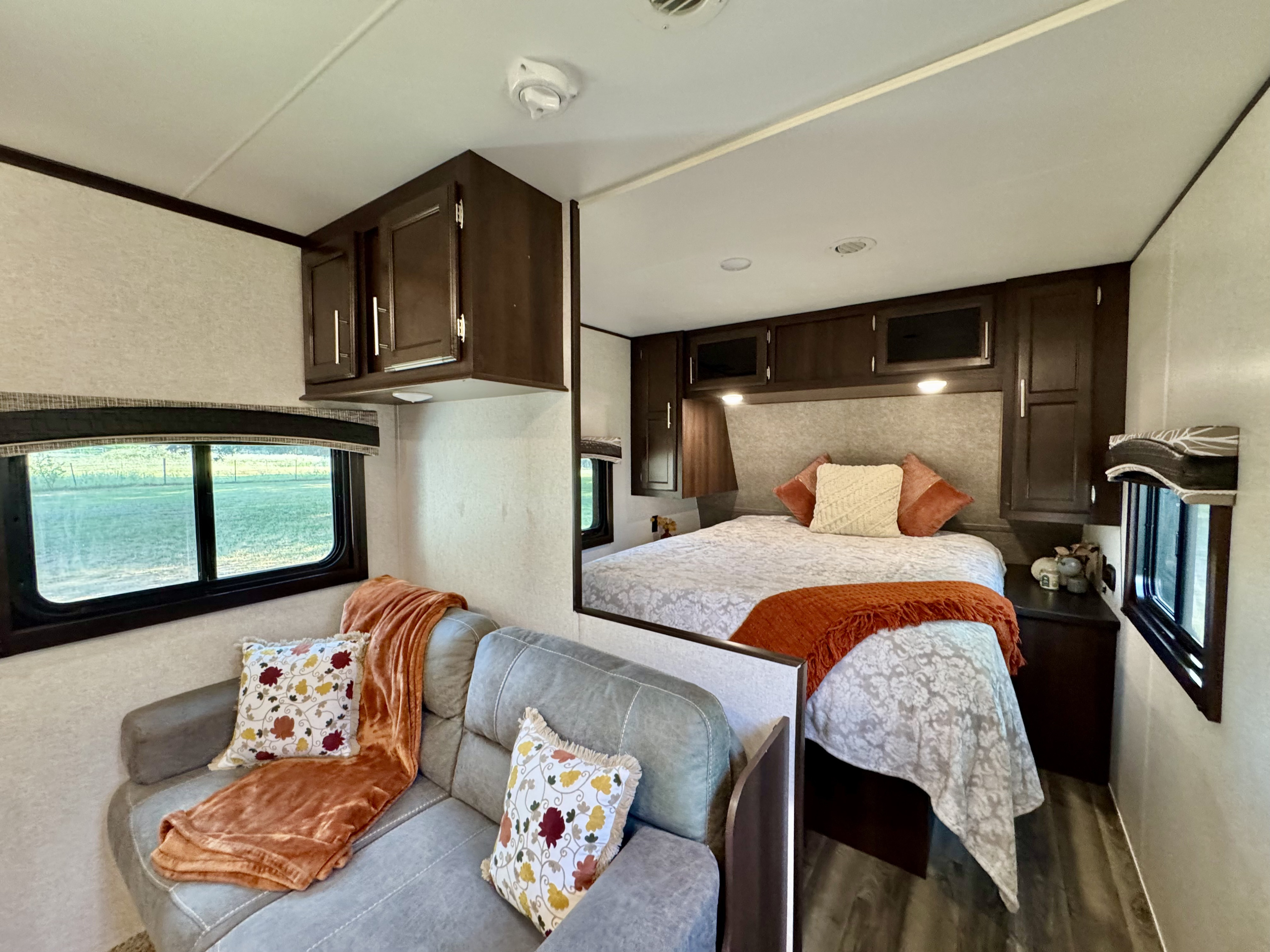 Cozy RV rental interior: a comfy living area with sofa & blankets, leading to a plush bedroom space. Dark wood cabinets throughout.. Jayco Jay Flight 2019