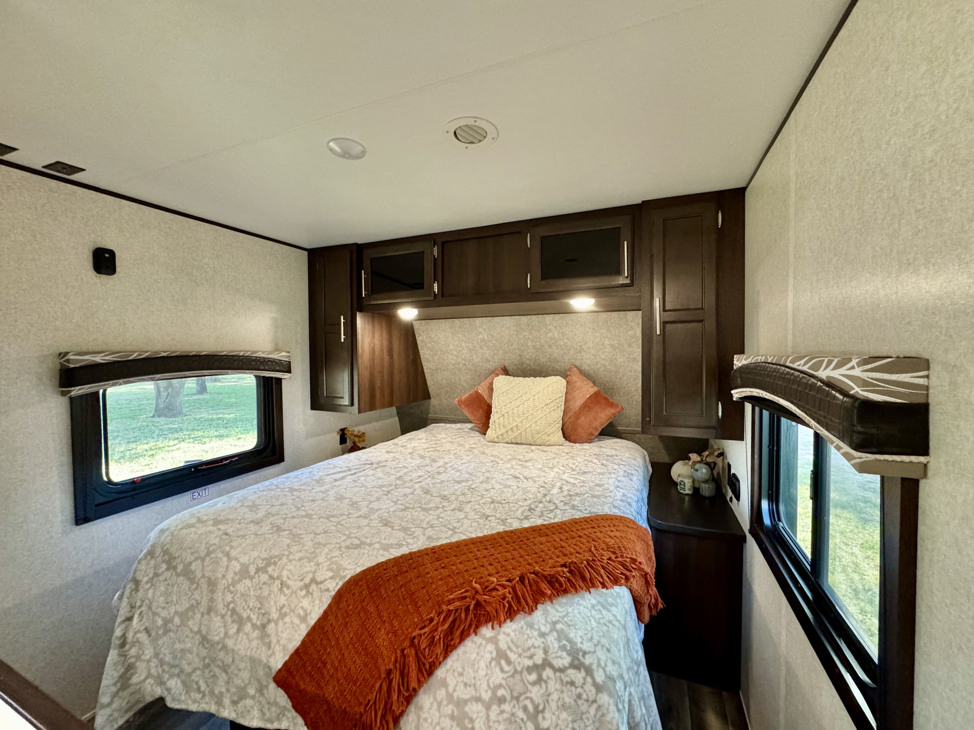 Experience comfort in this RV rental bedroom: cozy bed with orange throw, overhead cabinets, & two windows. Ideal for travel.. Jayco Jay Flight 2019