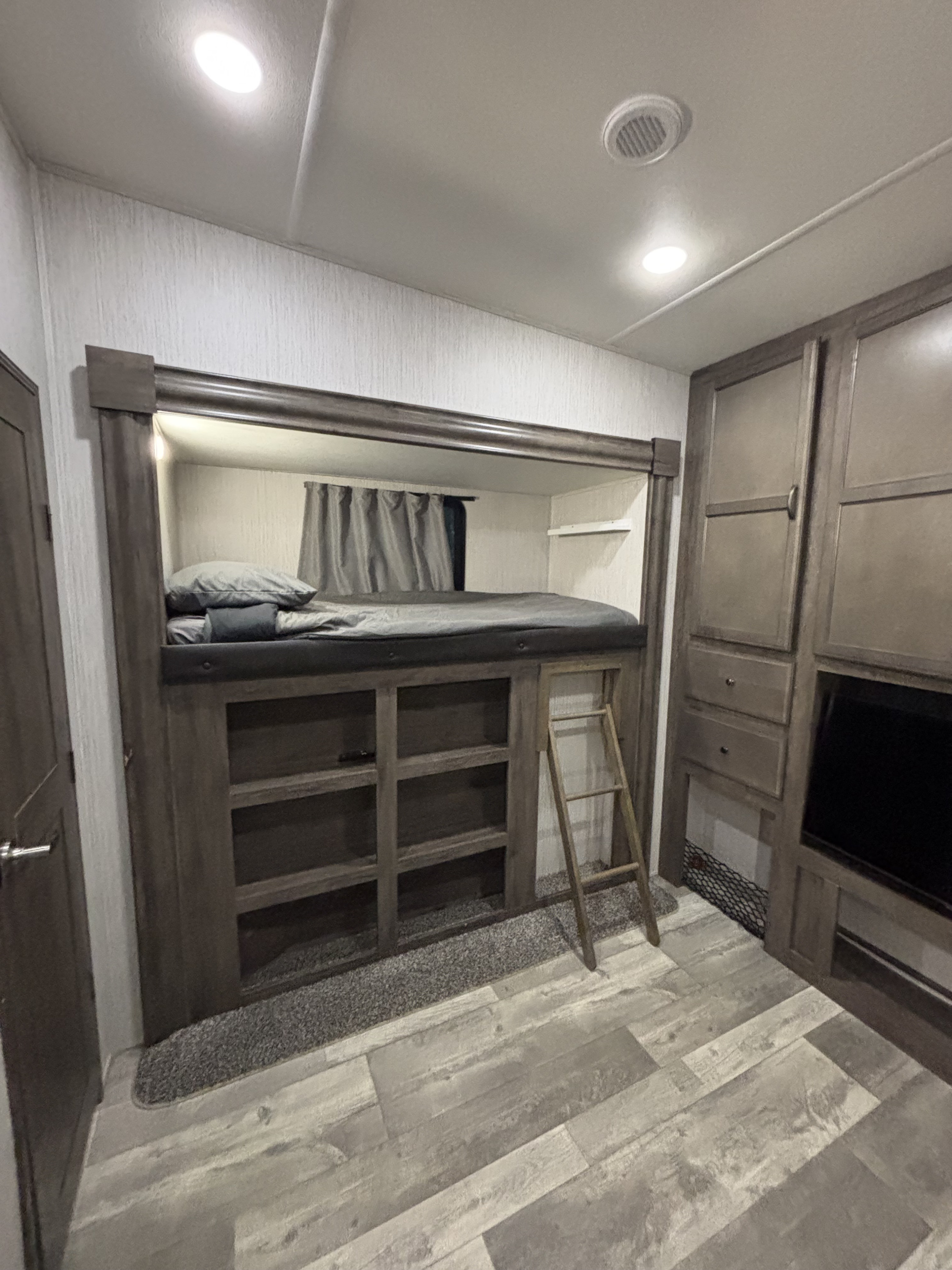 RV rental bunk bed with built-in storage, ladder, and adjacent cabinetry with TV. A practical and modern camper interior.. Forest River Sandpiper 2021