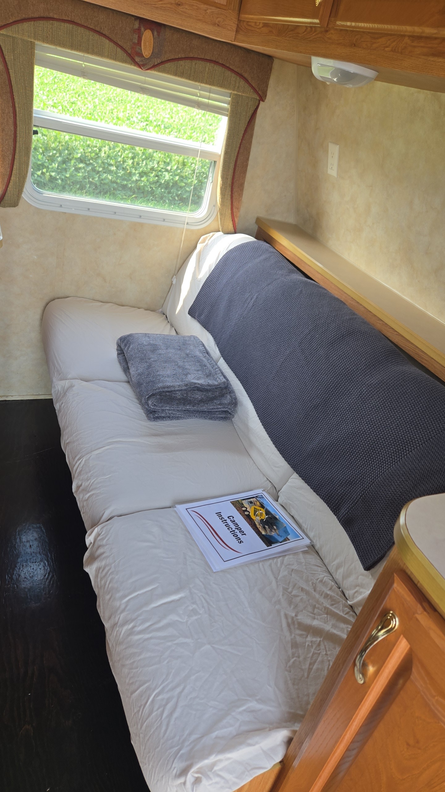 Cozy RV rental interior featuring a neatly made bed, blankets, and "Camper Instructions" by a bright window.. Jayco Jay Flight 2006