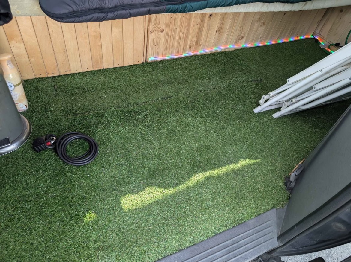 RV rental's cozy interior: artificial turf floor, wooden panels, colorful LED lights, and folded camping gear.. Dodge Grand Caravan Camper 2004