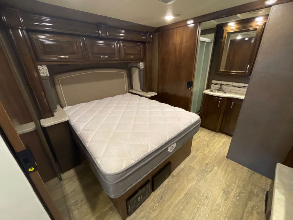 RV rental bedroom featuring a comfortable bed, overhead storage, and an attached compact bathroom with sink & shower.. Thor Chateau 2017
