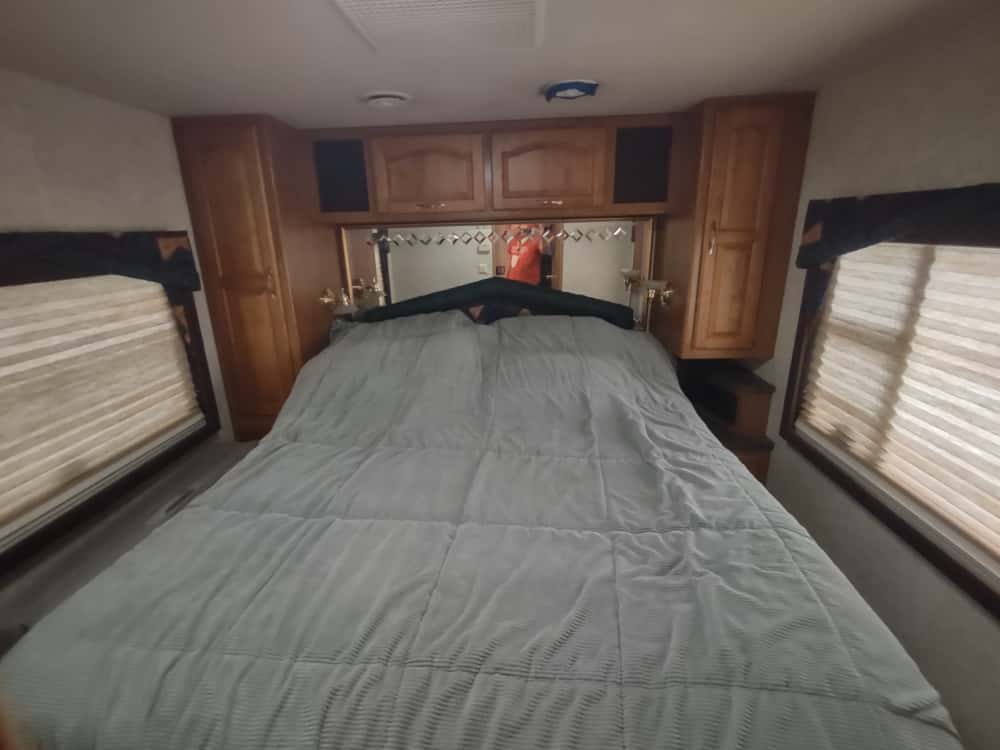Inside a comfortable RV rental bedroom featuring a spacious bed, wooden storage, and shaded windows.. Damon Corporation Ultrasport 2000