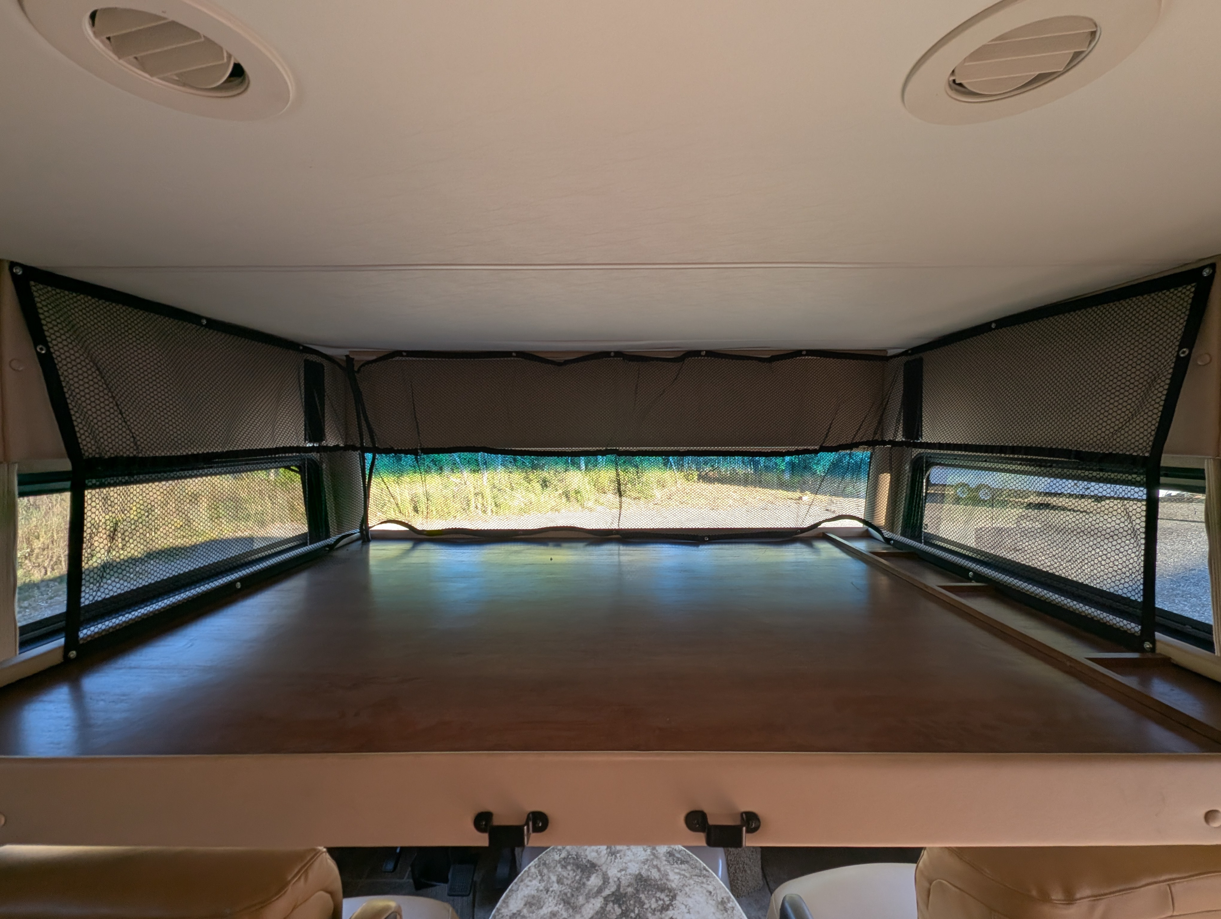 Inside an RV rental: a cozy overhead bunk with safety netting, visible windows showing trees, and ceiling vents for comfort.. Thor Miramar 2015