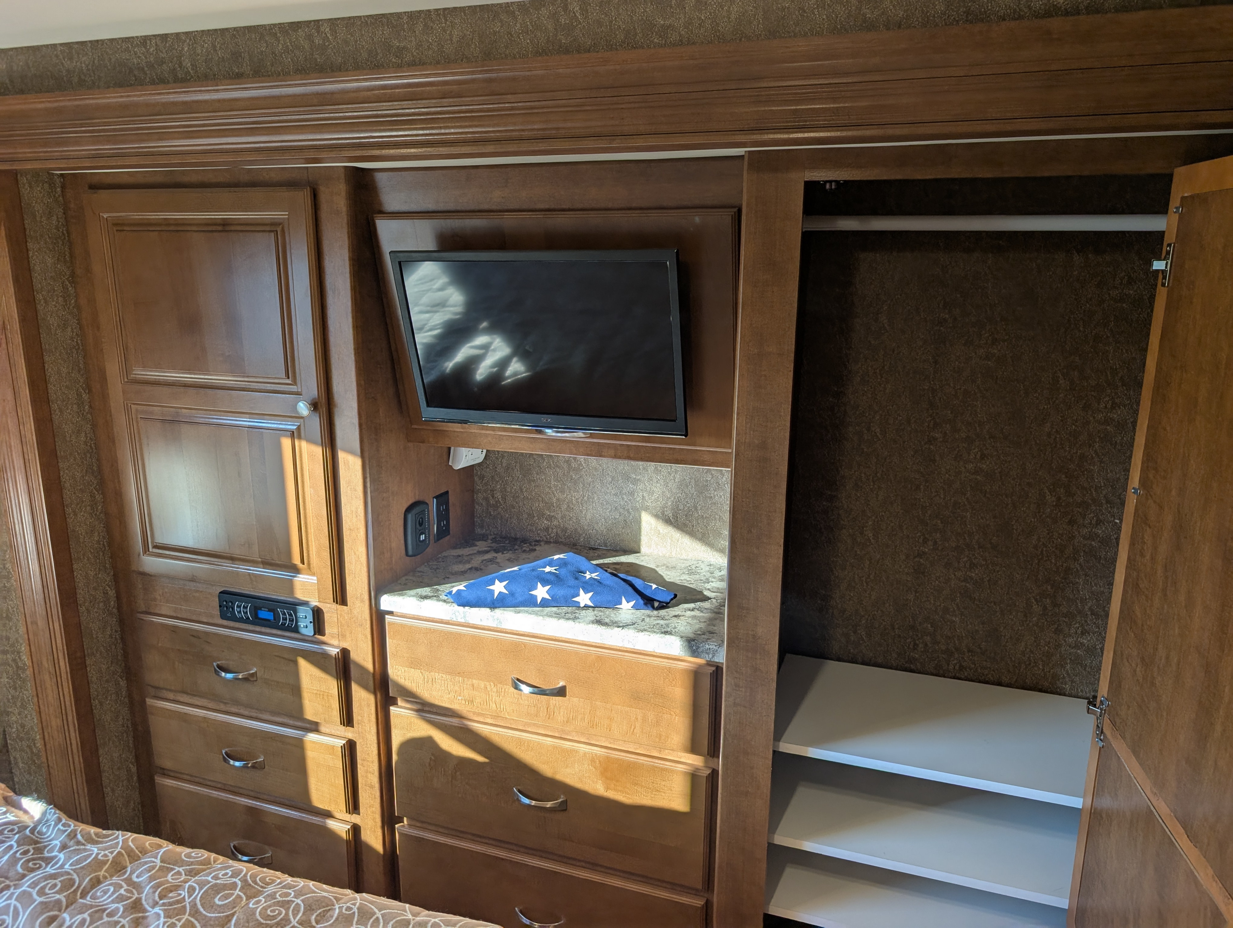 RV rental interior: wooden unit with TV, storage drawers, open closet with shelves, and a folded flag on the counter.. Thor Miramar 2015