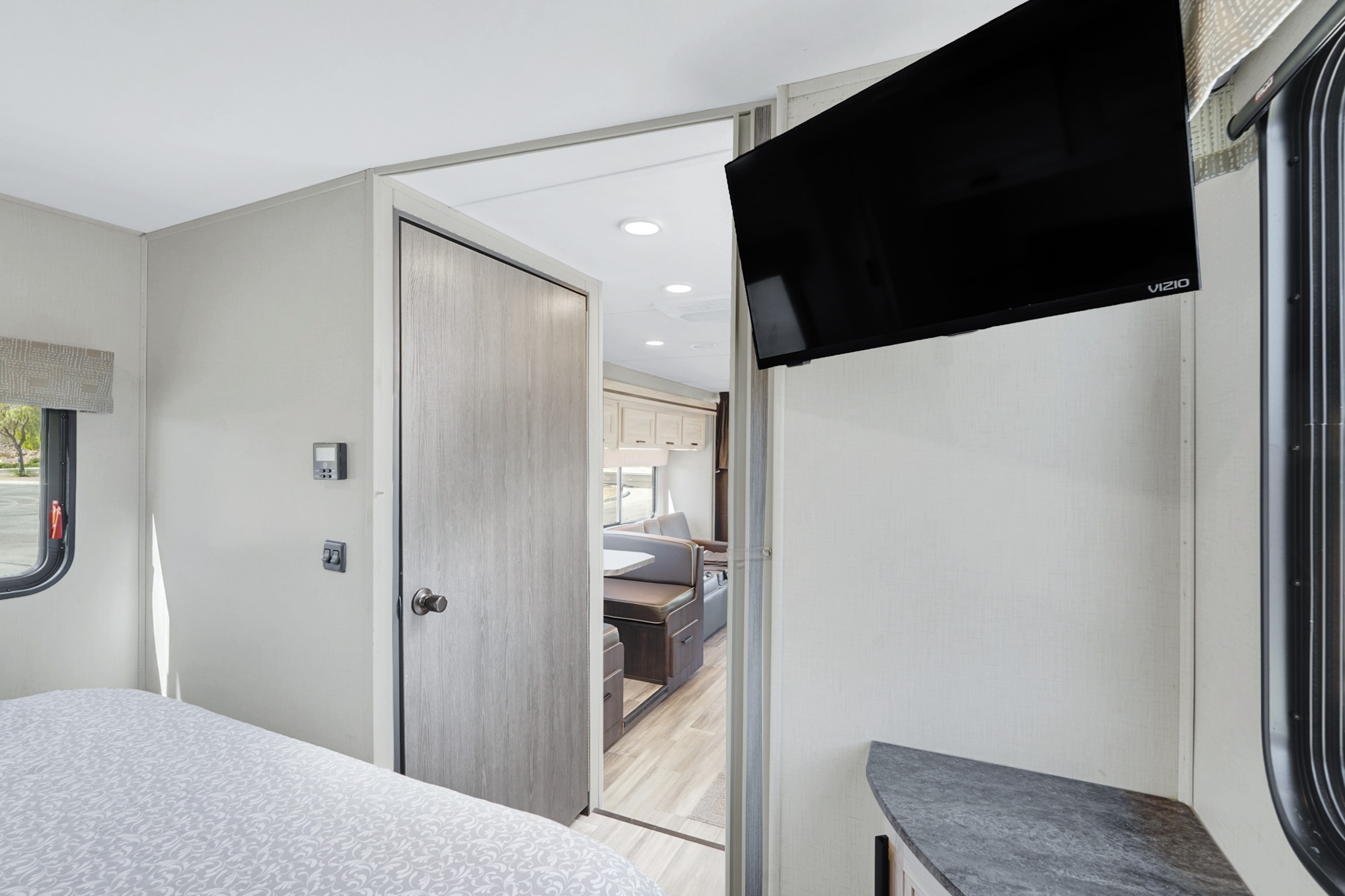 Bright RV rental interior featuring a bedroom with a mounted TV, and a doorway to the dinette and kitchen.. Forest River Sunseeker LE 2023