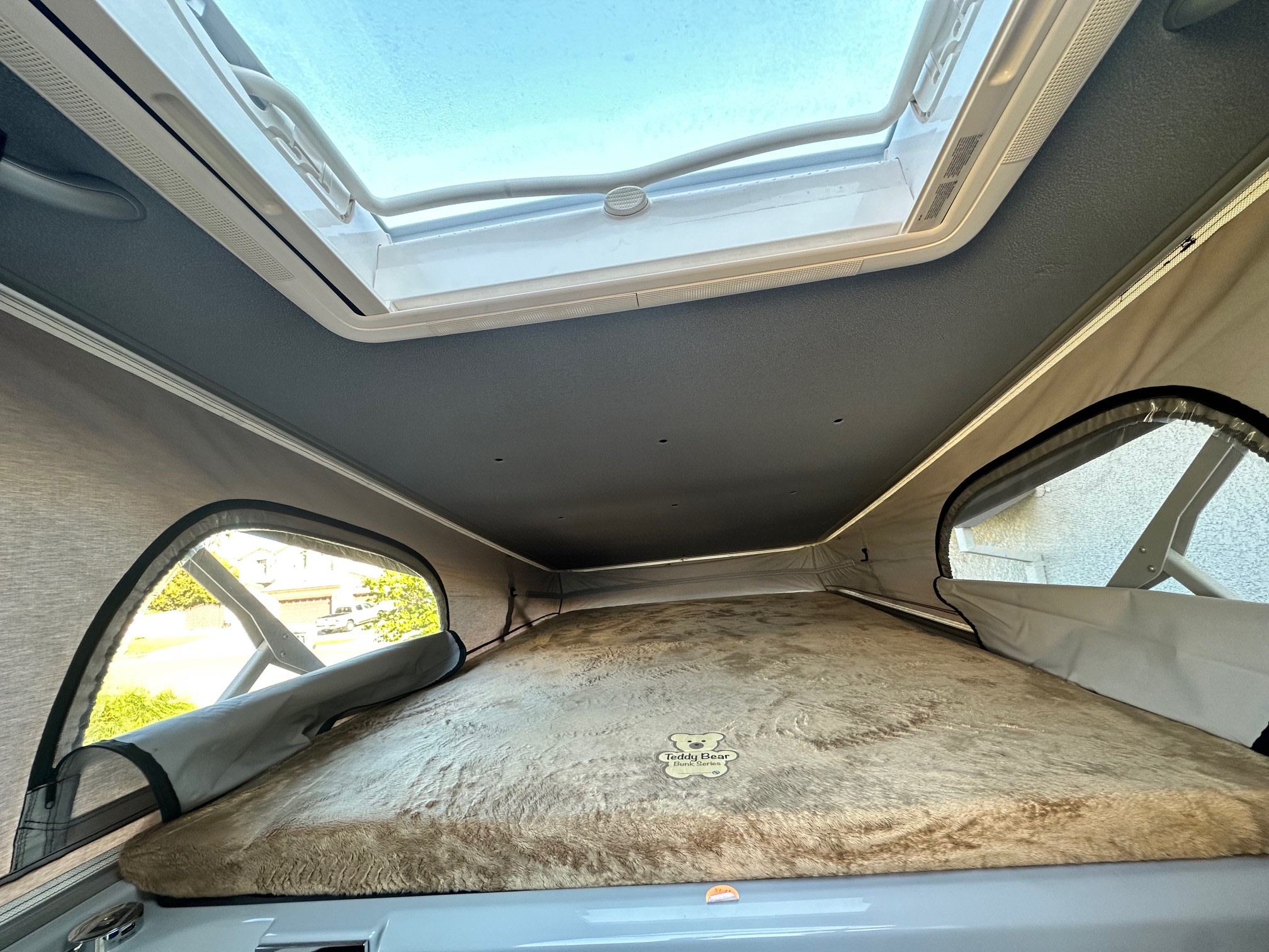 Cozy RV rental pop-top bed featuring a plush "Teddy Bear Bunk Series" mattress and a bright overhead skylight.. Thor Motor Coach Tellaro 20J 2025