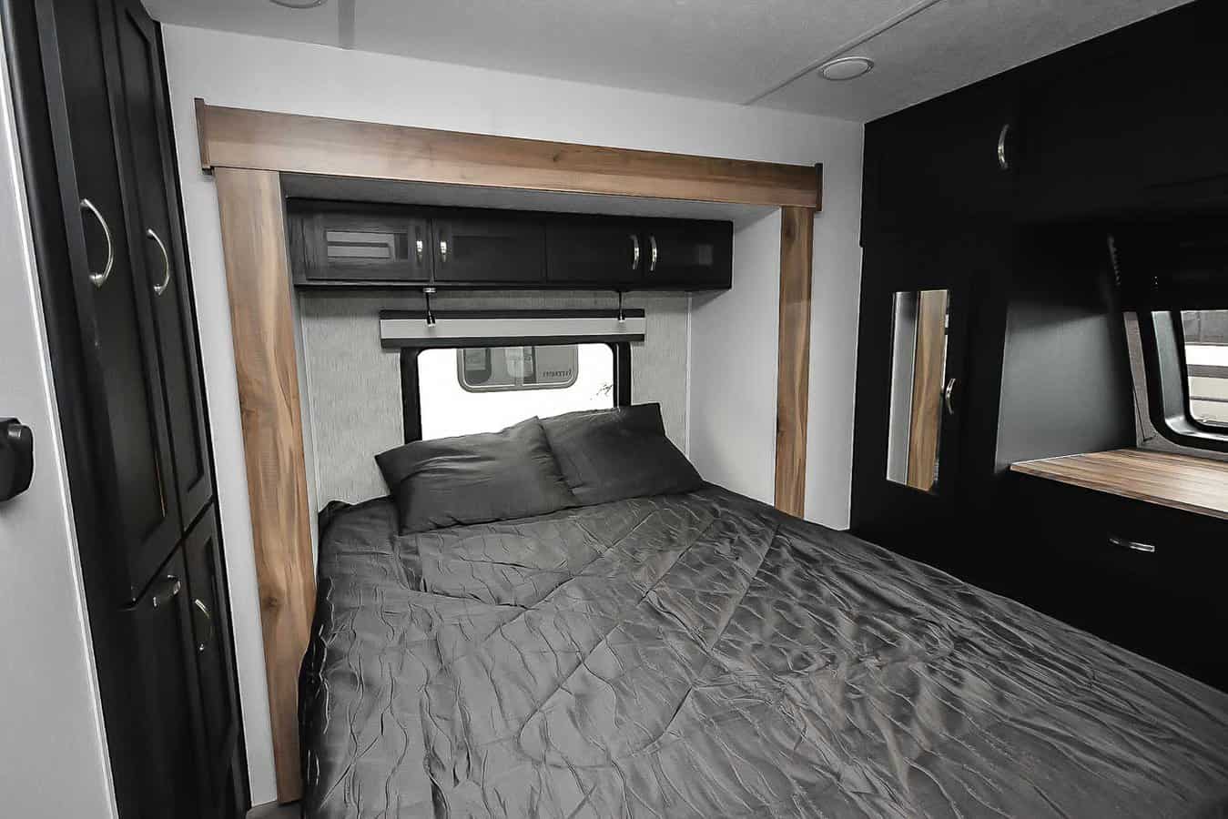 Cozy RV rental bedroom with dark grey bedding, overhead cabinets, a window, and stylish wood trim for comfort.. Coachmen Coachmen Freedom Express Liberty Edition (324RLDSLE) 2022