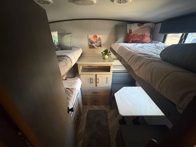 RV rental's cozy bunk bed area: two sets of beds, a central storage cabinet, and a pull-out table for travelers.. Cruiser RV Shadow Cruiser 2021