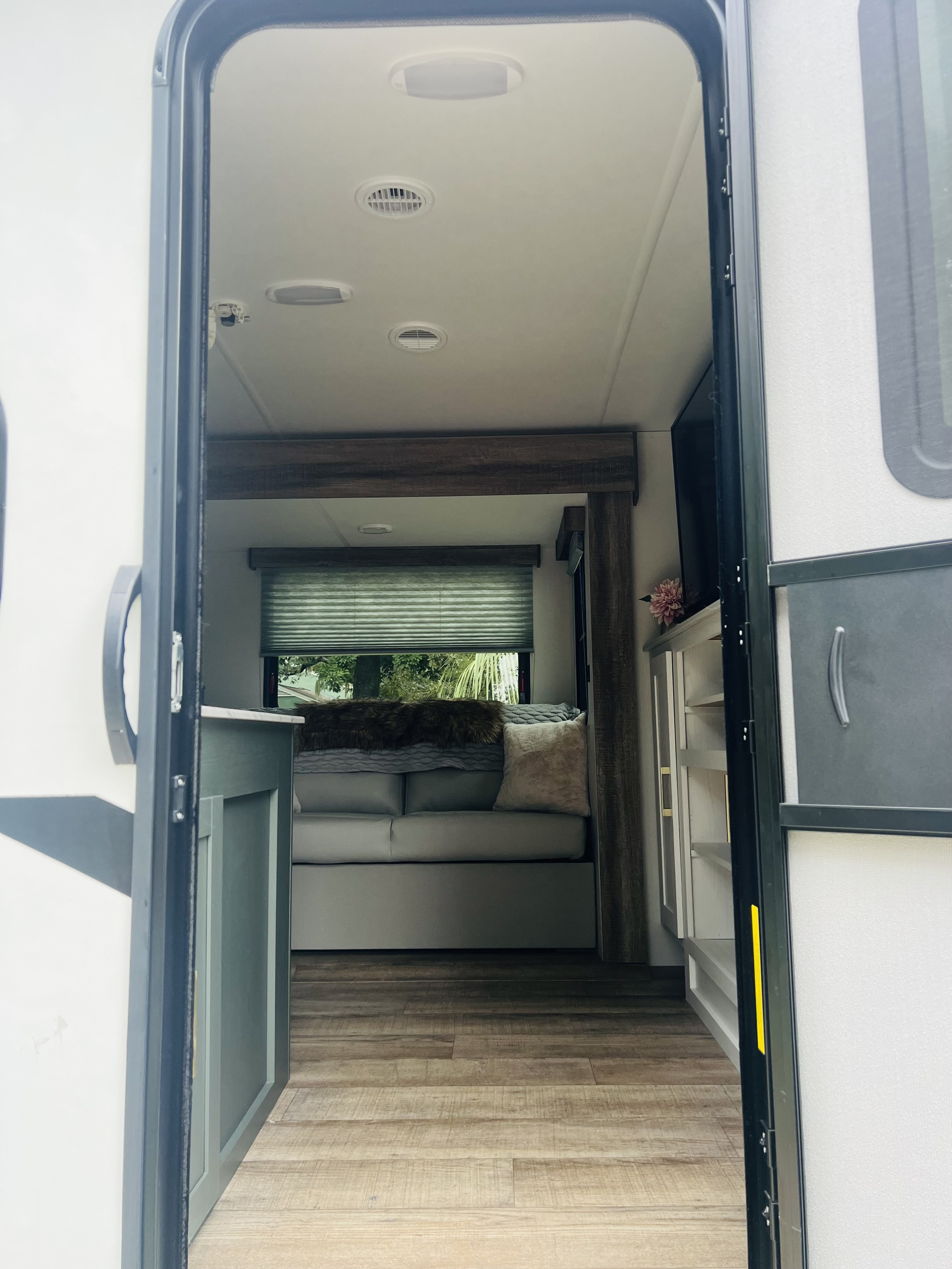 Open RV rental door reveals a cozy living space with sofa, window, wood-look flooring, and built-in cabinets.. Heartland RVs 265BH-L 2024