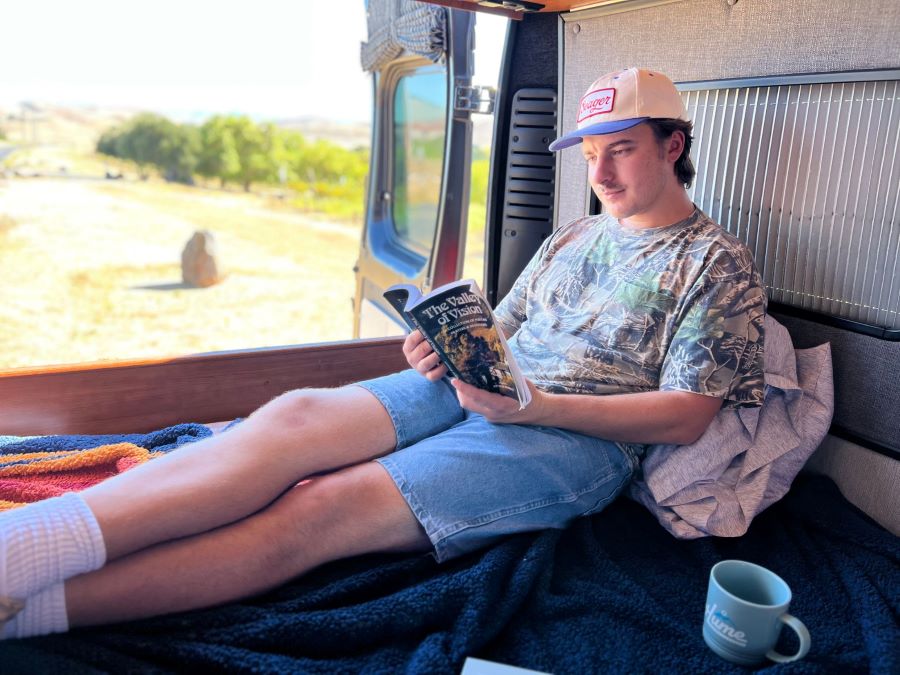 Man relaxes reading "The Valley of Vision" in an RV rental, overlooking a scenic landscape. Ideal for a serene getaway.. Roadtrek Roadtrek Class B 2017