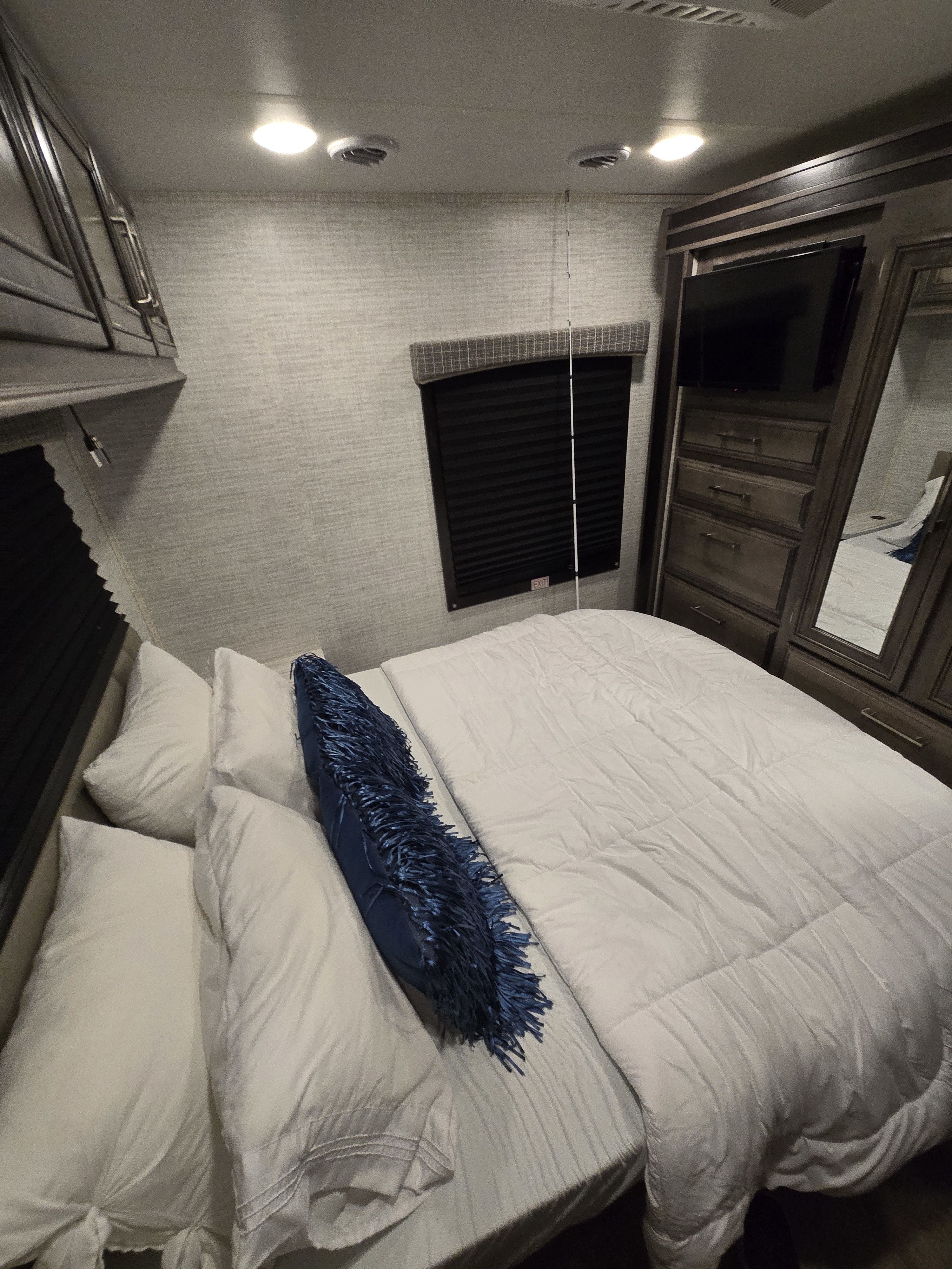 This inviting RV rental bedroom features a comfy bed with white bedding, a modern TV, and ample storage, perfect for road trips.. Entegra Coach Odyssey 2024