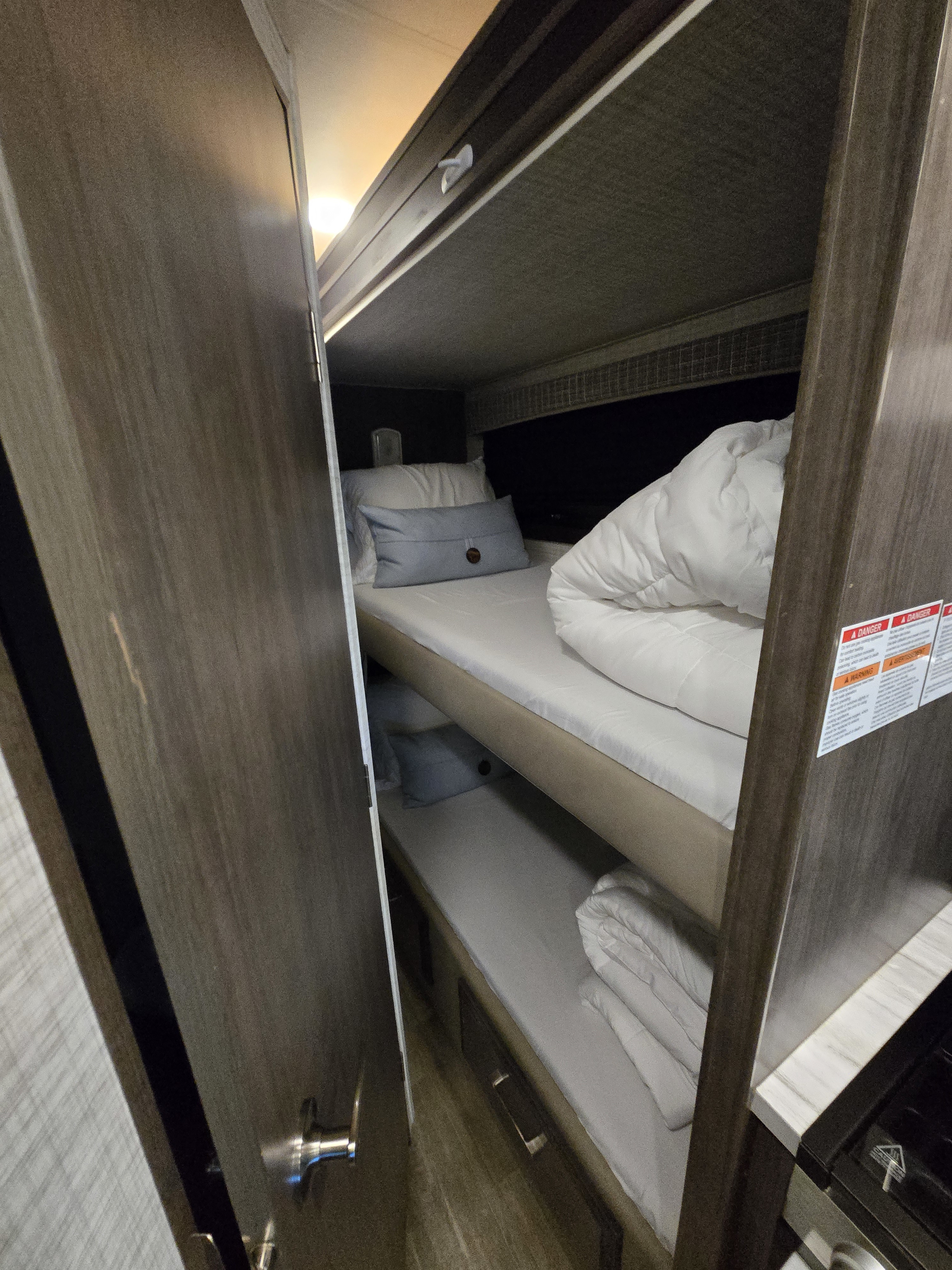 View of an rv rental's cozy bunk beds. Two bunks are neatly made with white bedding; the top has a blue accent pillow. Compact sleeping area.. Entegra Coach Odyssey 2024