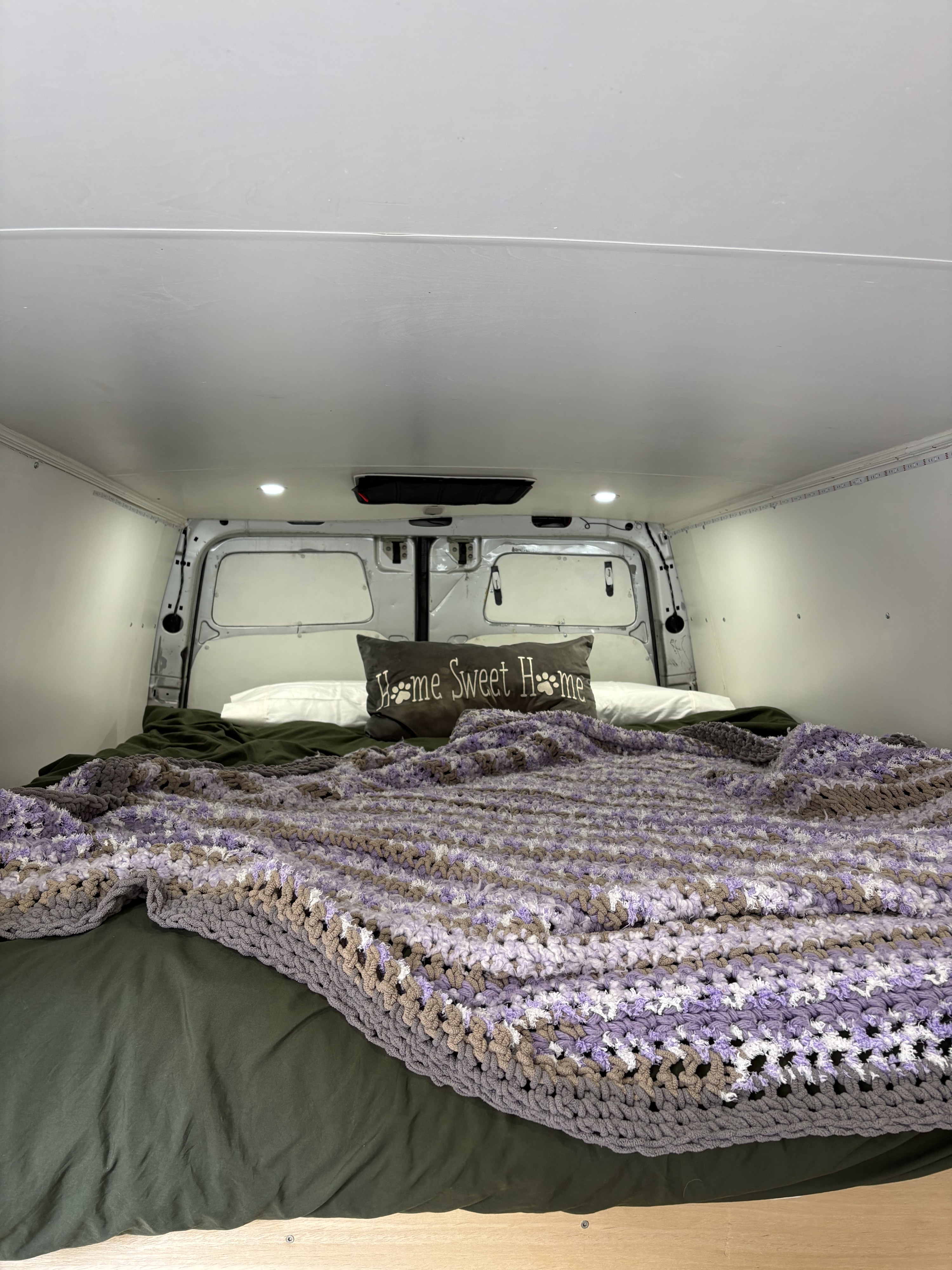 Inside this cozy RV rental: a comfy bed with a "Home Sweet Home" pillow and a purple crocheted blanket.. Mercedes Sprinter 2014
