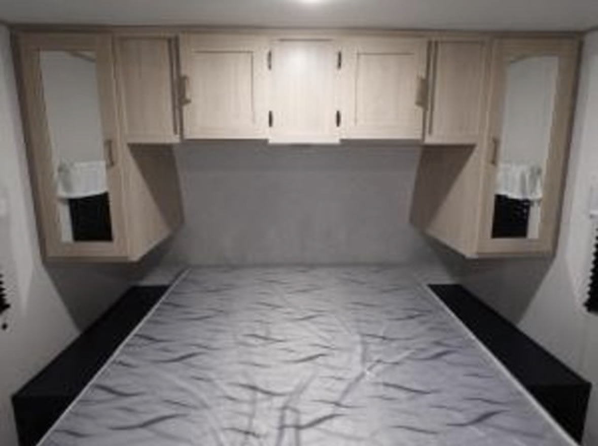 Cozy RV rental bedroom features a comfy bed, overhead cabinets, and mirrored wardrobes for your travel comfort.. Prime Time Avenger 2025