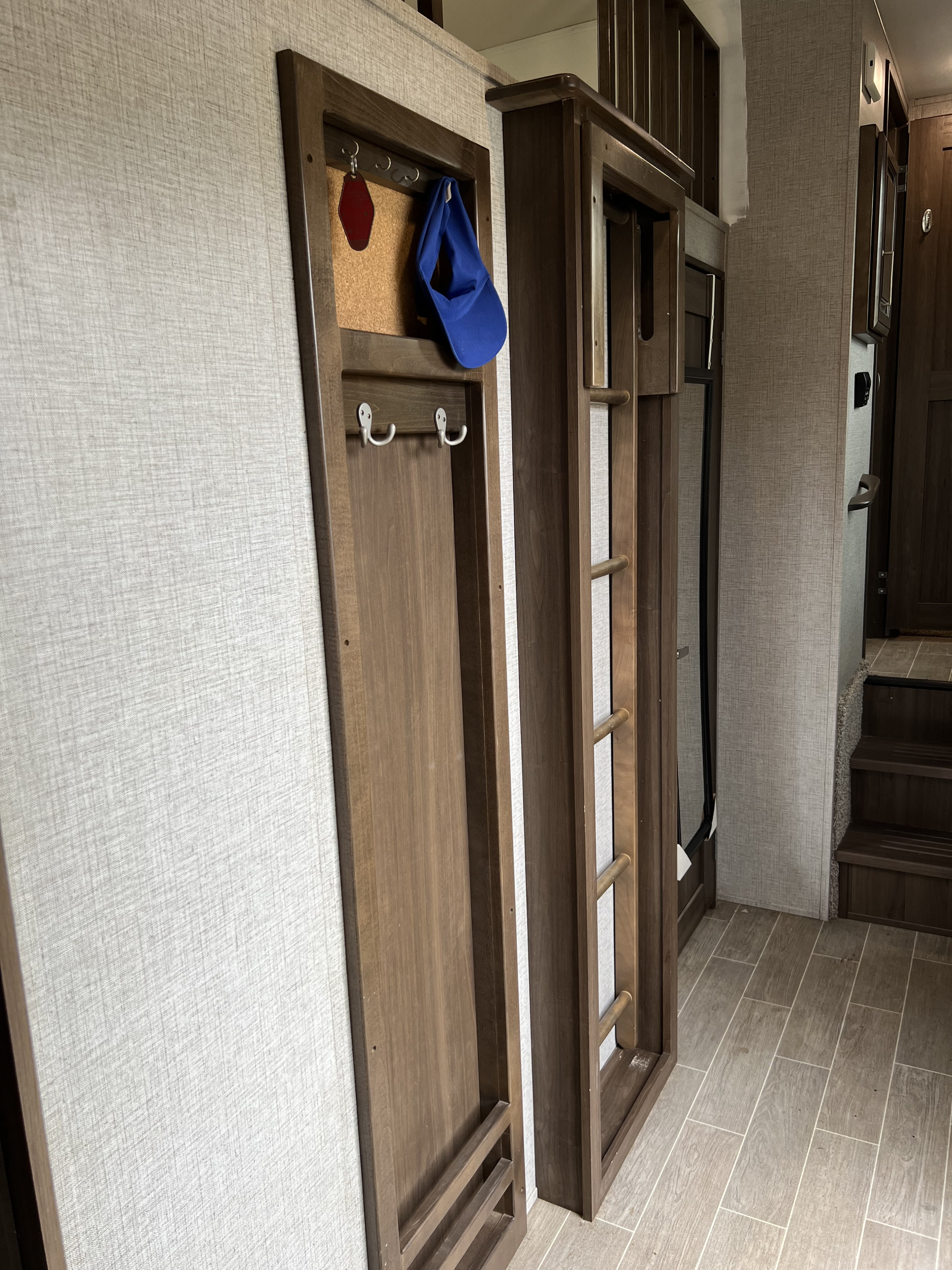 RV rental interior shows light wall paneling, a wooden key/hat rack, a bunk ladder, tiled flooring, and stairs in the background.. Keystone RV Avalanche 2019