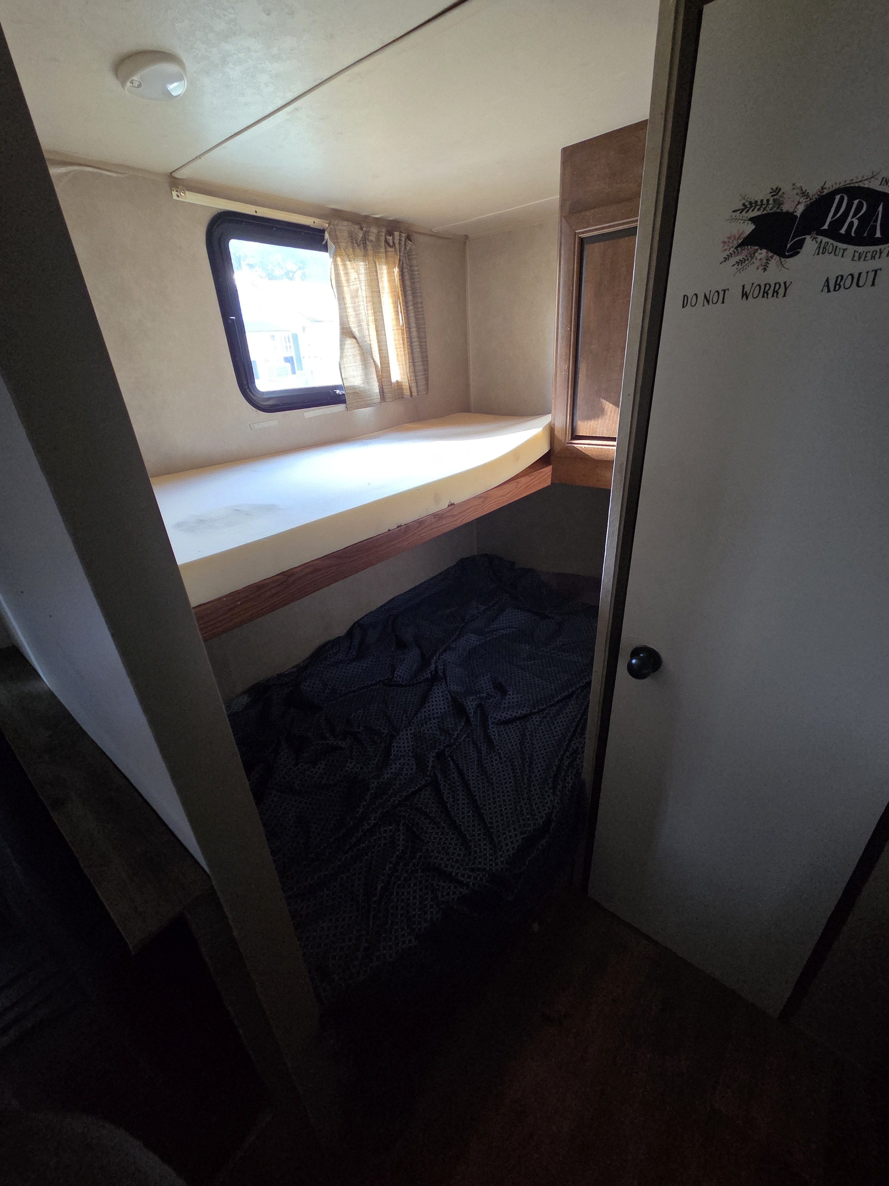 This cozy RV rental interior features stacked bunk beds, with an upper foam mattress and a lower bed covered by a dark blanket.. Forest River Salem Cruise Lite 2017