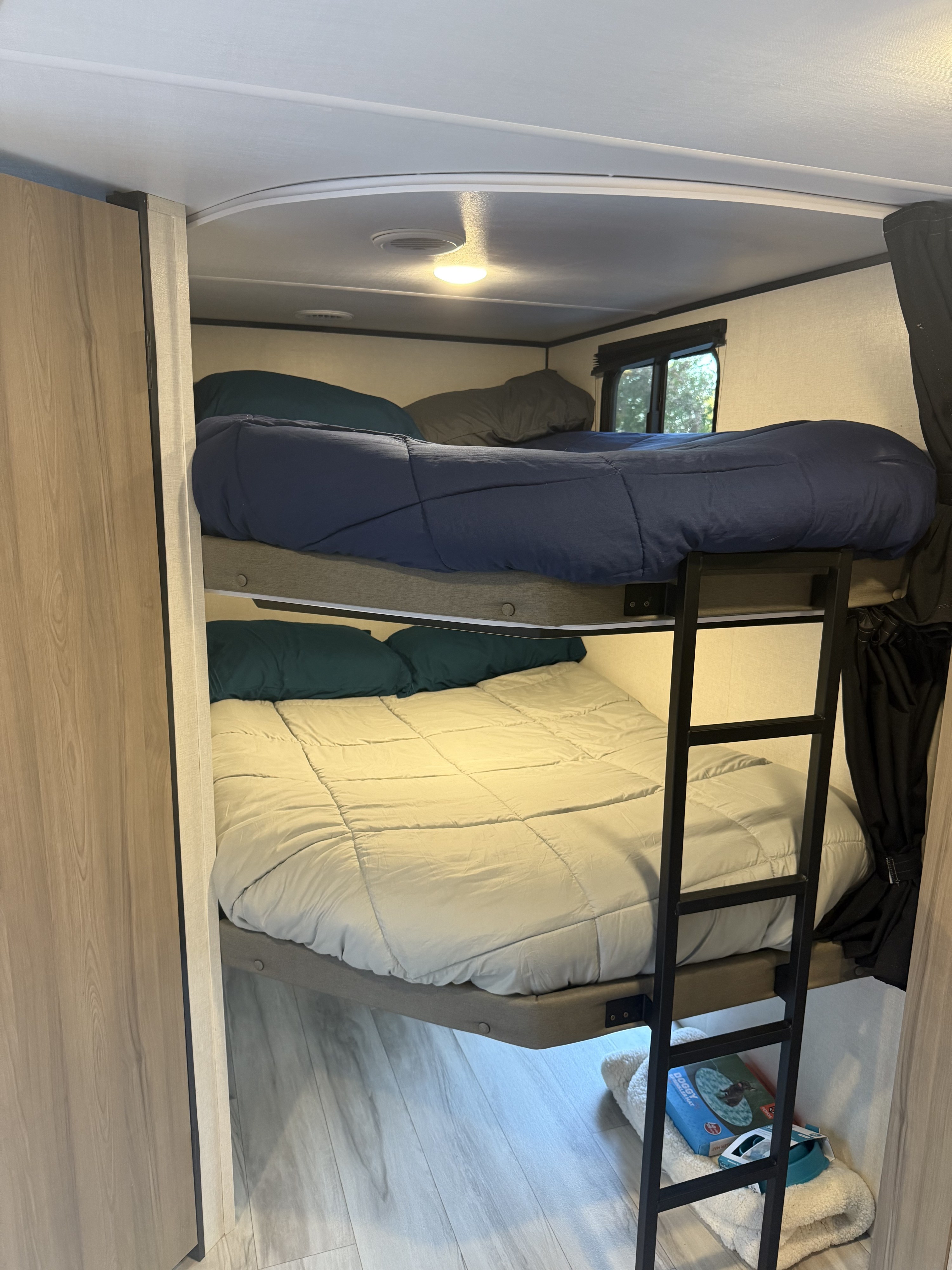 This RV rental offers a cozy bunk bed setup. The upper bunk has blue bedding, the lower has beige, with a ladder for access.. Keystone RV Keystone Coleman Light 22BX 2025
