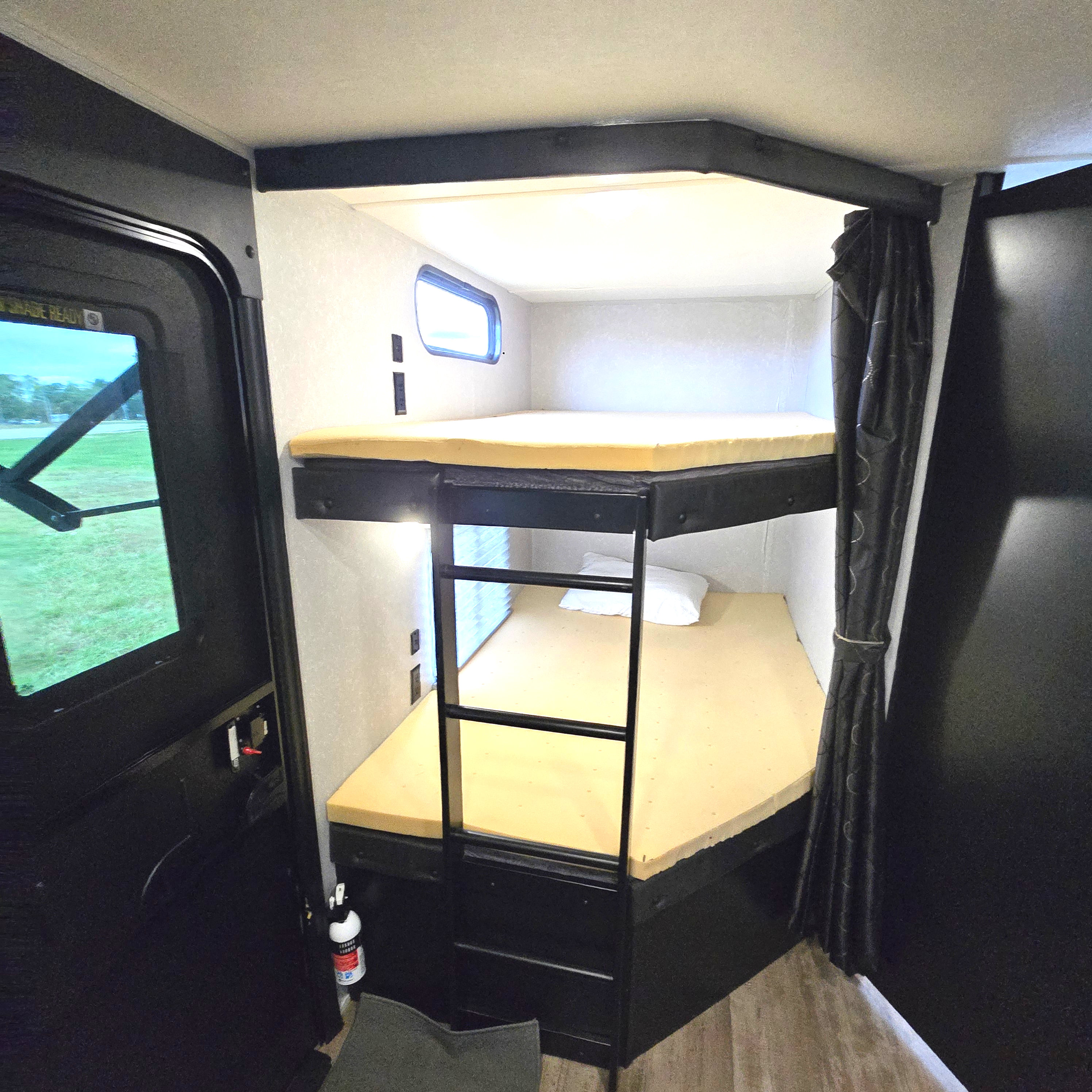 RV rental interior: bunk beds with foam mattresses, ladder, small window, and dark curtain for sleeping arrangements.. Forest River Cherokee Limited 2021