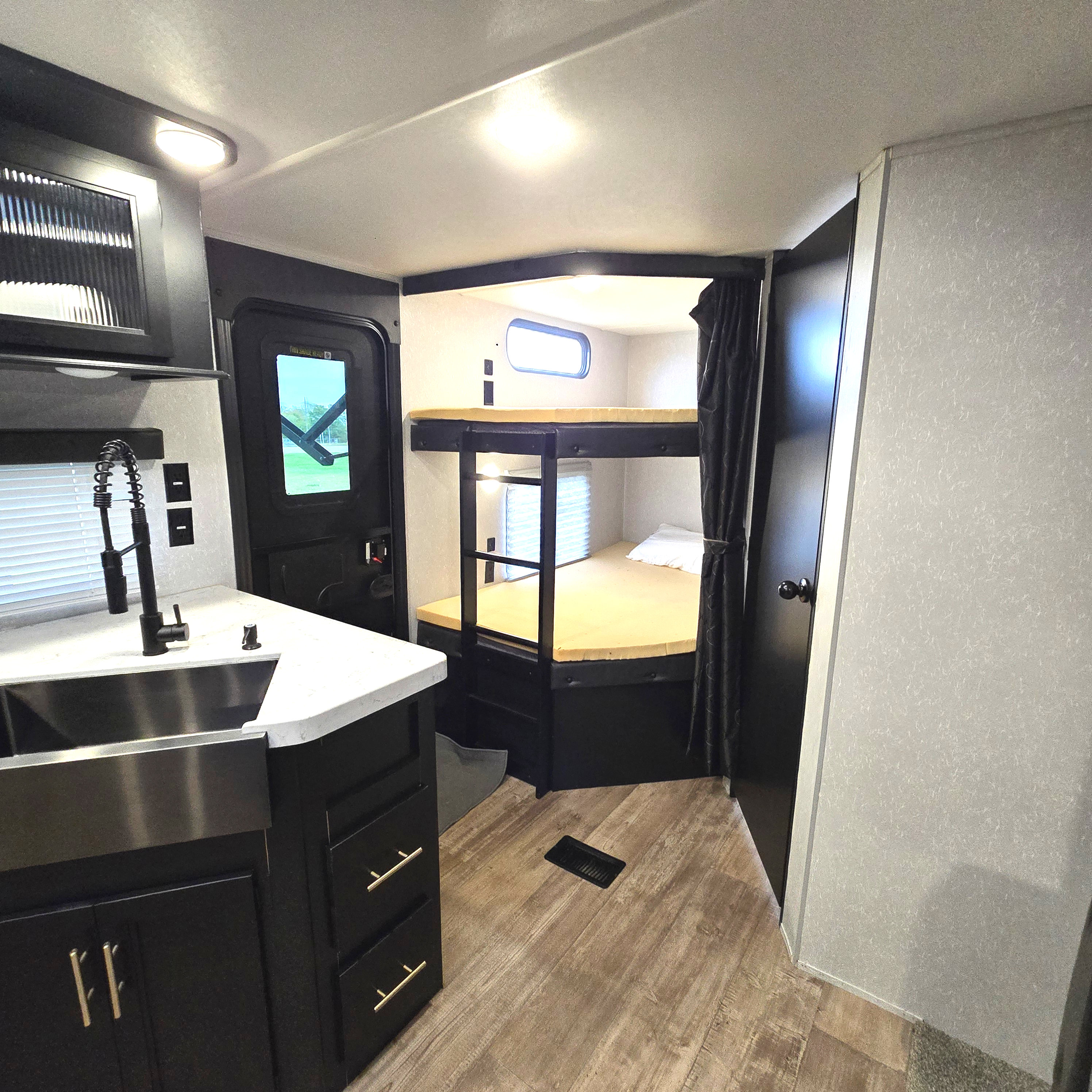 Spacious RV rental interior featuring a modern kitchen with a sink, bunk beds with a privacy curtain, and wood-look flooring.. Forest River Cherokee Limited 2021