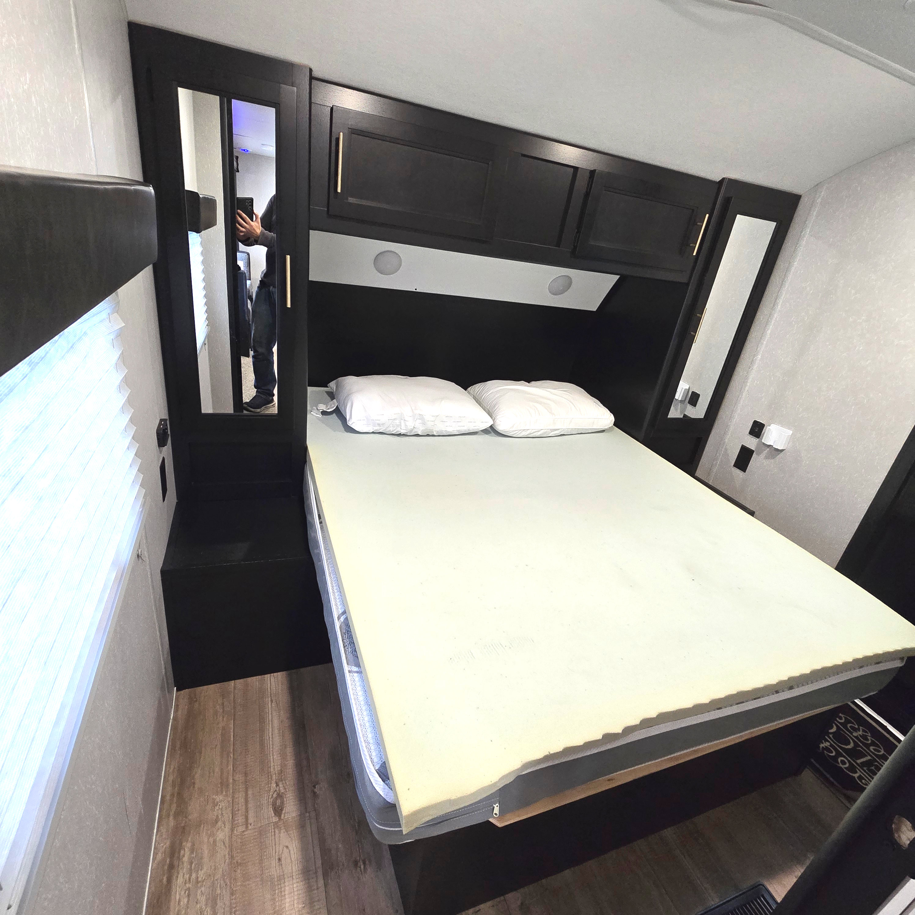 Compact RV rental bedroom featuring a bed with memory foam topper, overhead storage, and modern dark wood finishes.. Forest River Cherokee Limited 2021