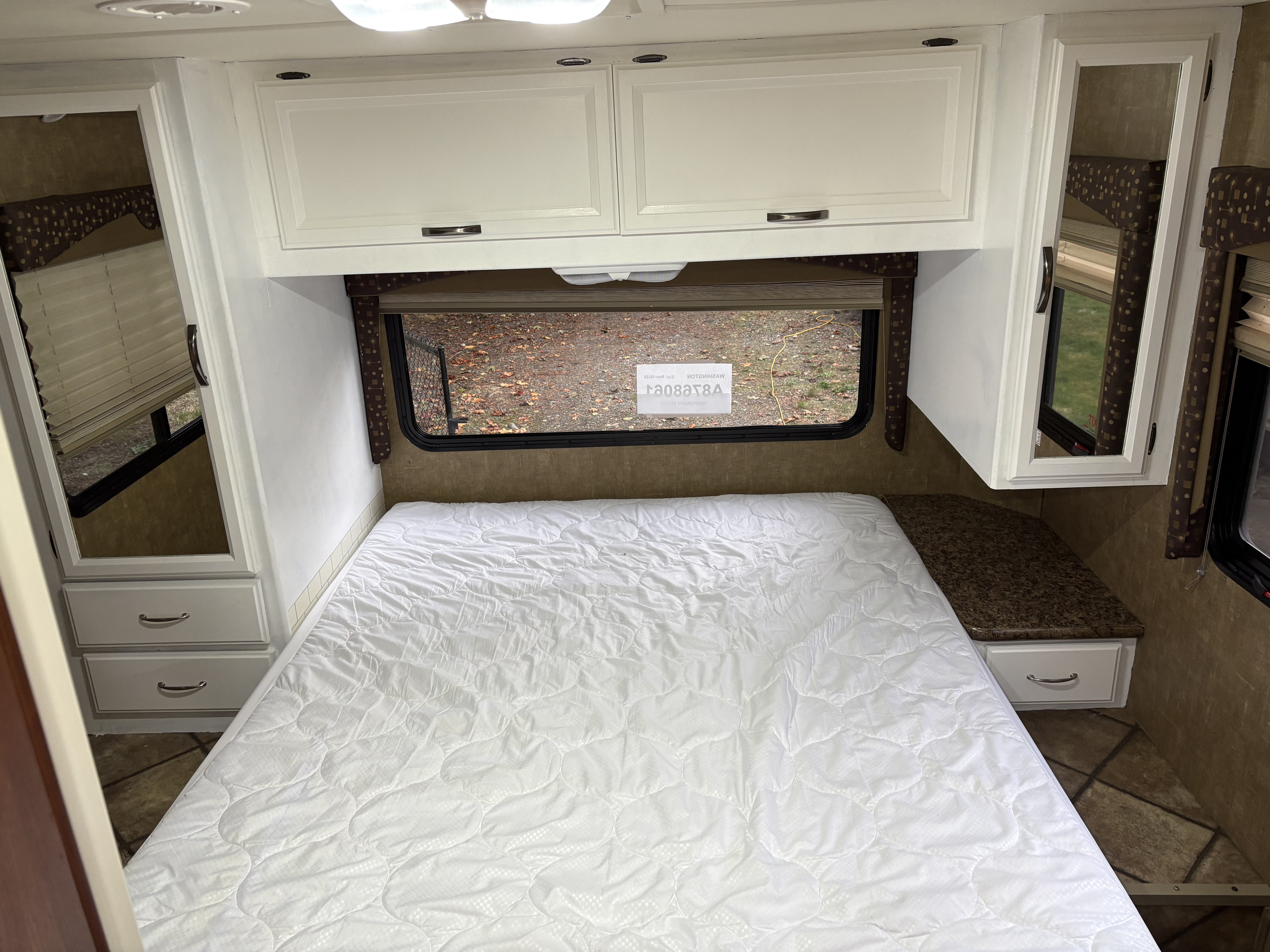 Comfortable RV rental bedroom featuring a white bed, overhead cabinets, window, and mirrored storage. Ideal for travel.. Thor Freedom Elite 2014