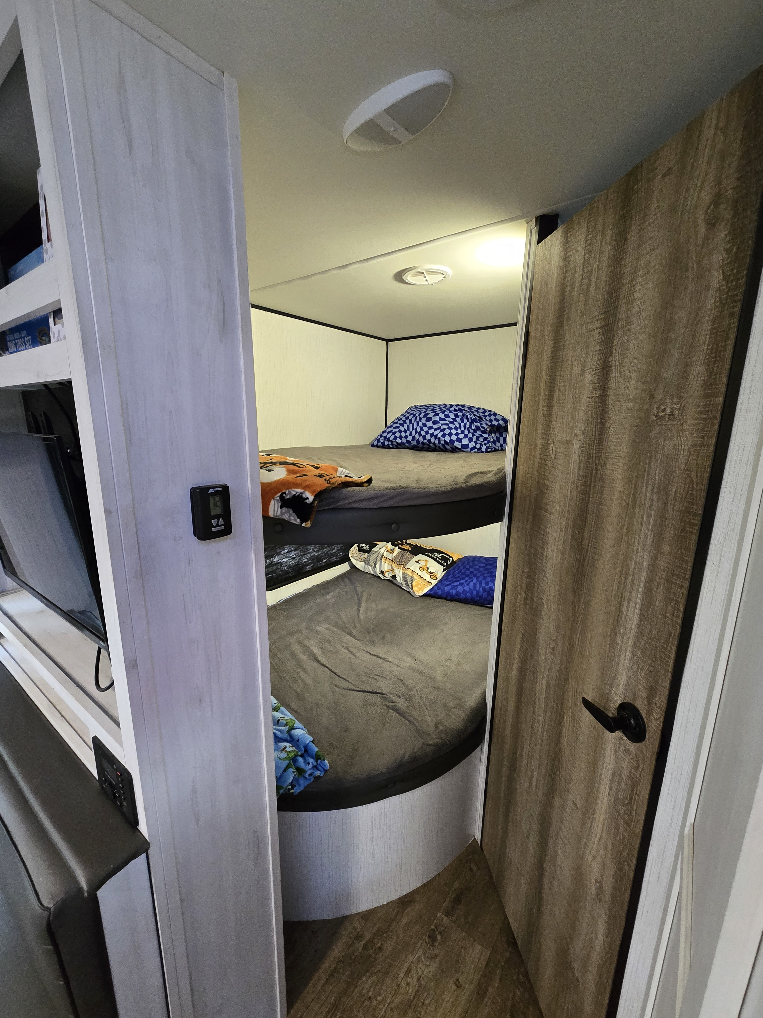 Cozy RV rental interior featuring two bunk beds with soft bedding, a wall-mounted thermostat, and a TV entertainment unit.. Heartland RVs Trail Runner 2022