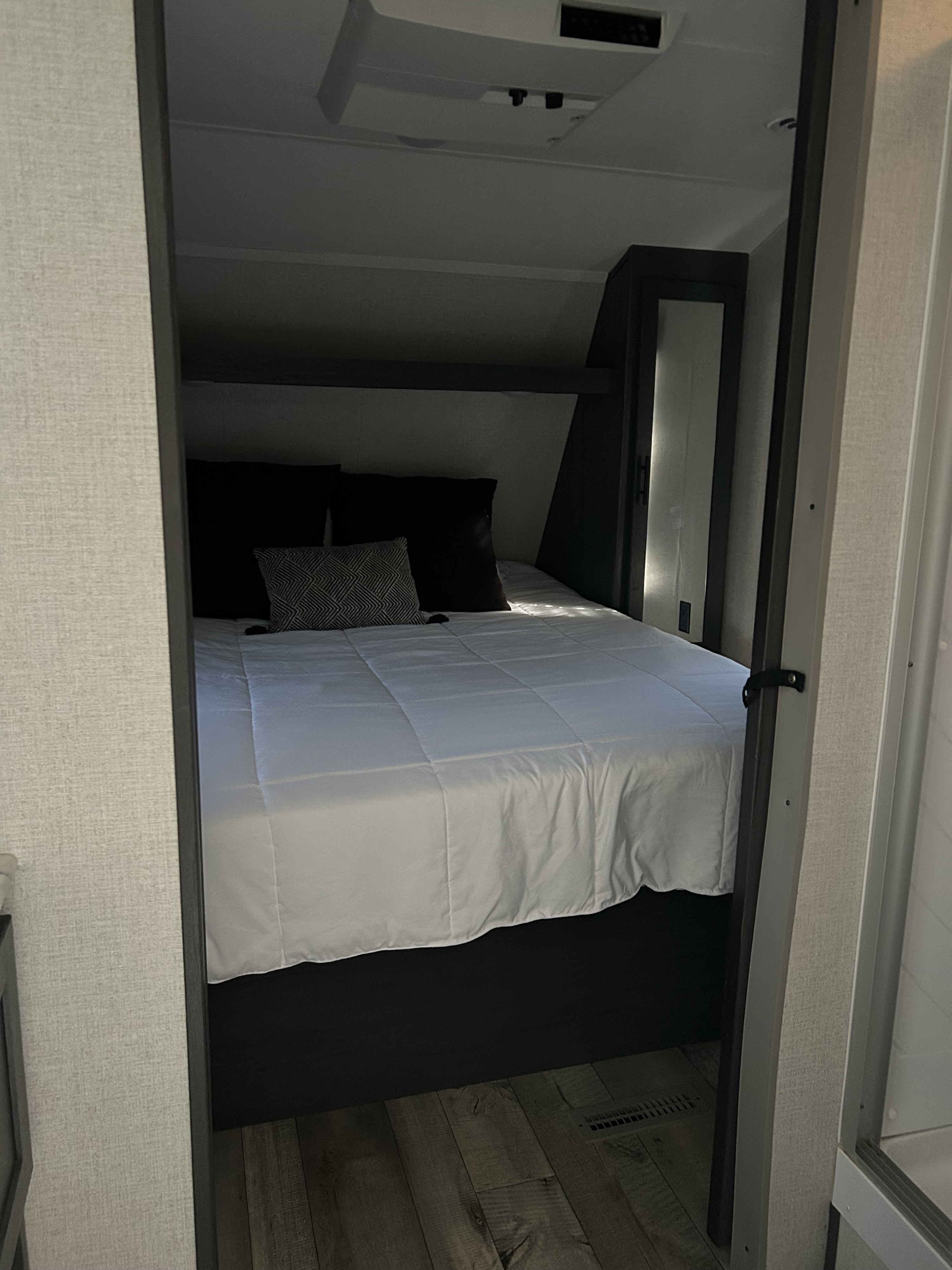 Step into a cozy, compact RV rental bedroom with a neatly made bed, white bedding, dark pillows, and wood flooring.. Dutchmen 3120BHS 2021
