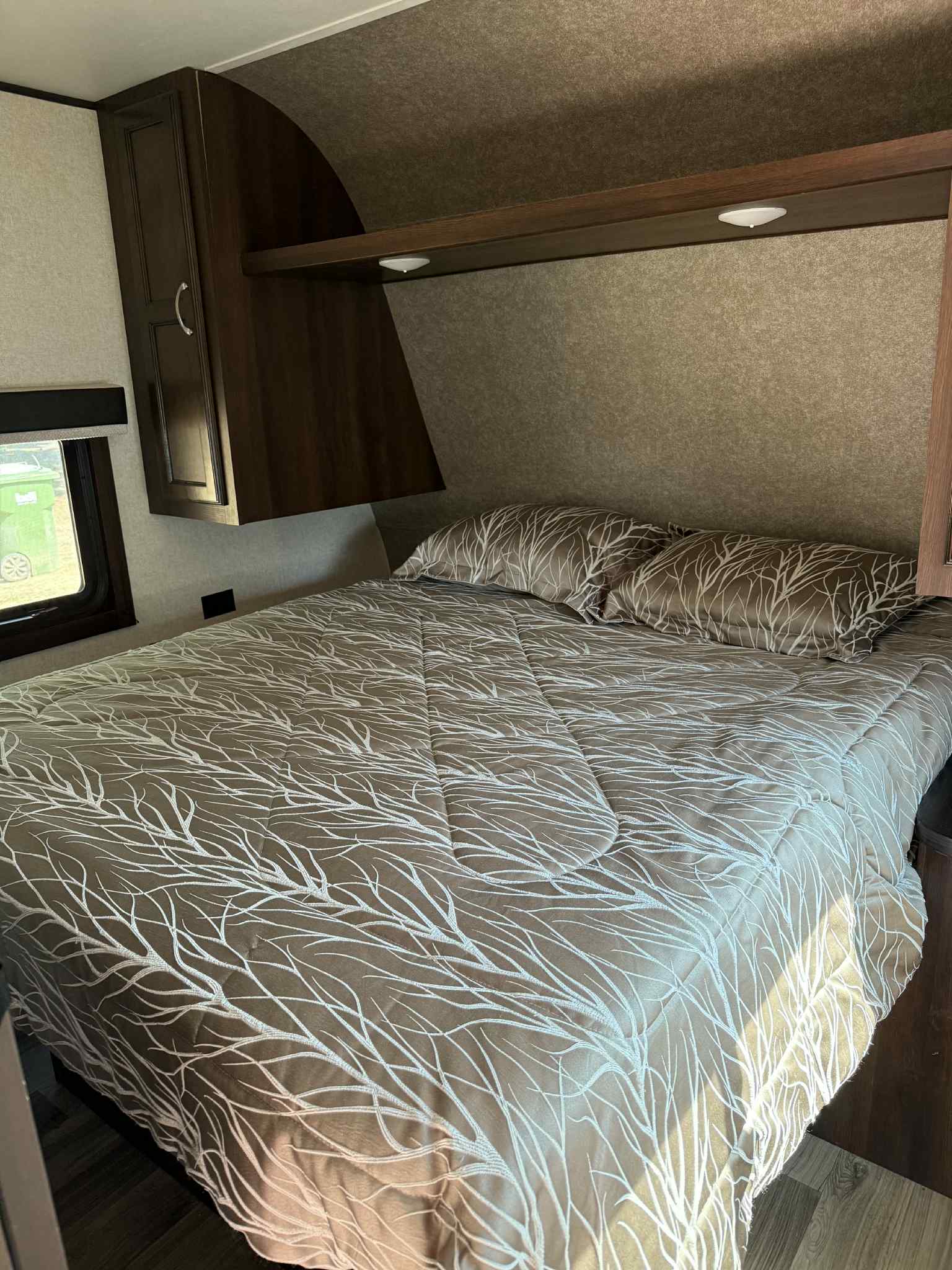 Spacious RV rental bedroom with a comfortable bed, earthy branch-patterned bedding, dark wood cabinets, and shelf lighting.. Jayco Jay Flight SLX Rocky Mountain Edition 2018