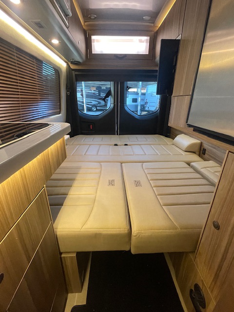 Modern RV rental interior featuring a comfortable, beige convertible bed, sleek kitchenette, and wood accents.. Airstream Interstate 2023