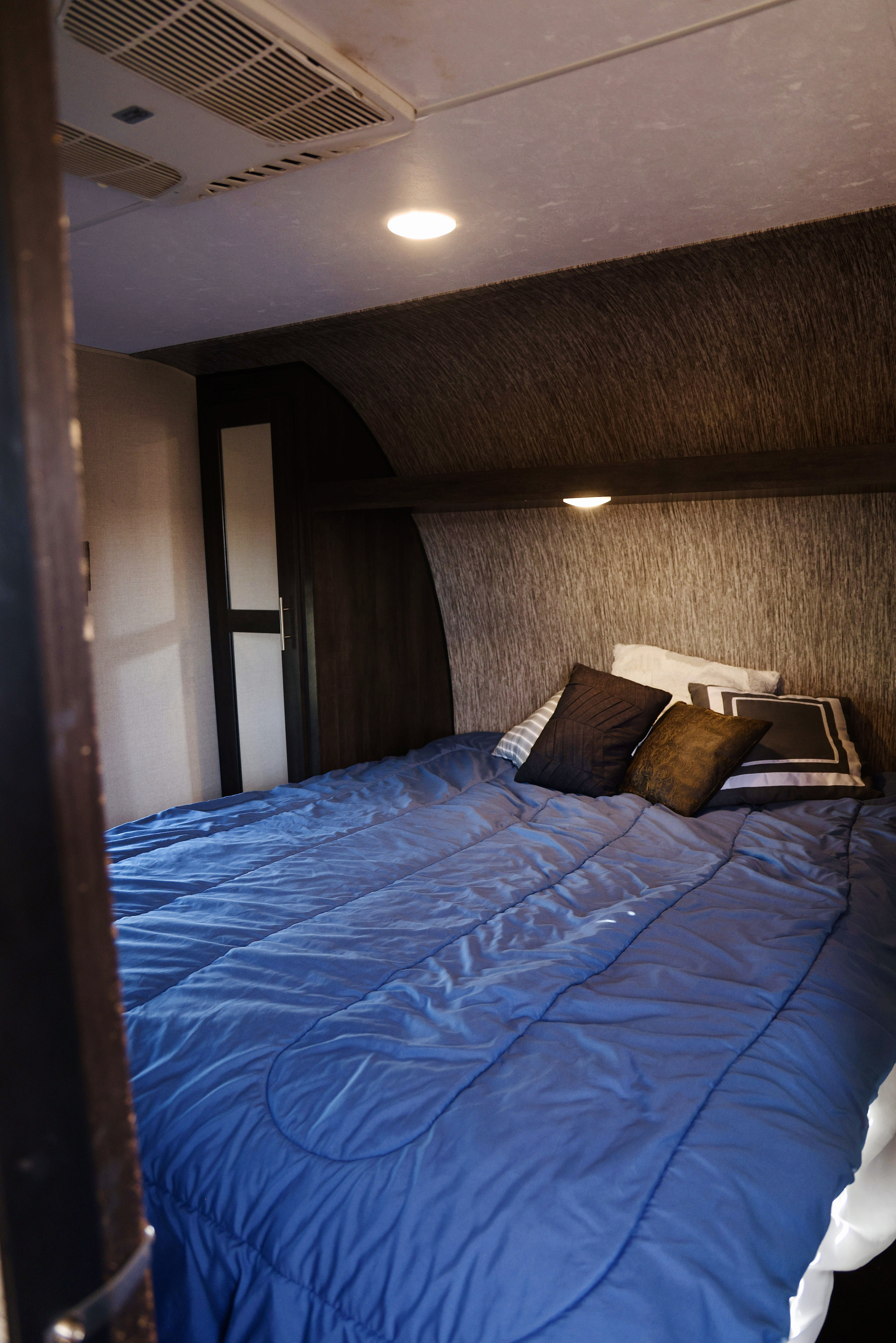 Inside a cozy RV rental bedroom: blue comforter, plush pillows, ceiling AC, and accent lighting for a comfy stay.. Sportsmen SE 2019