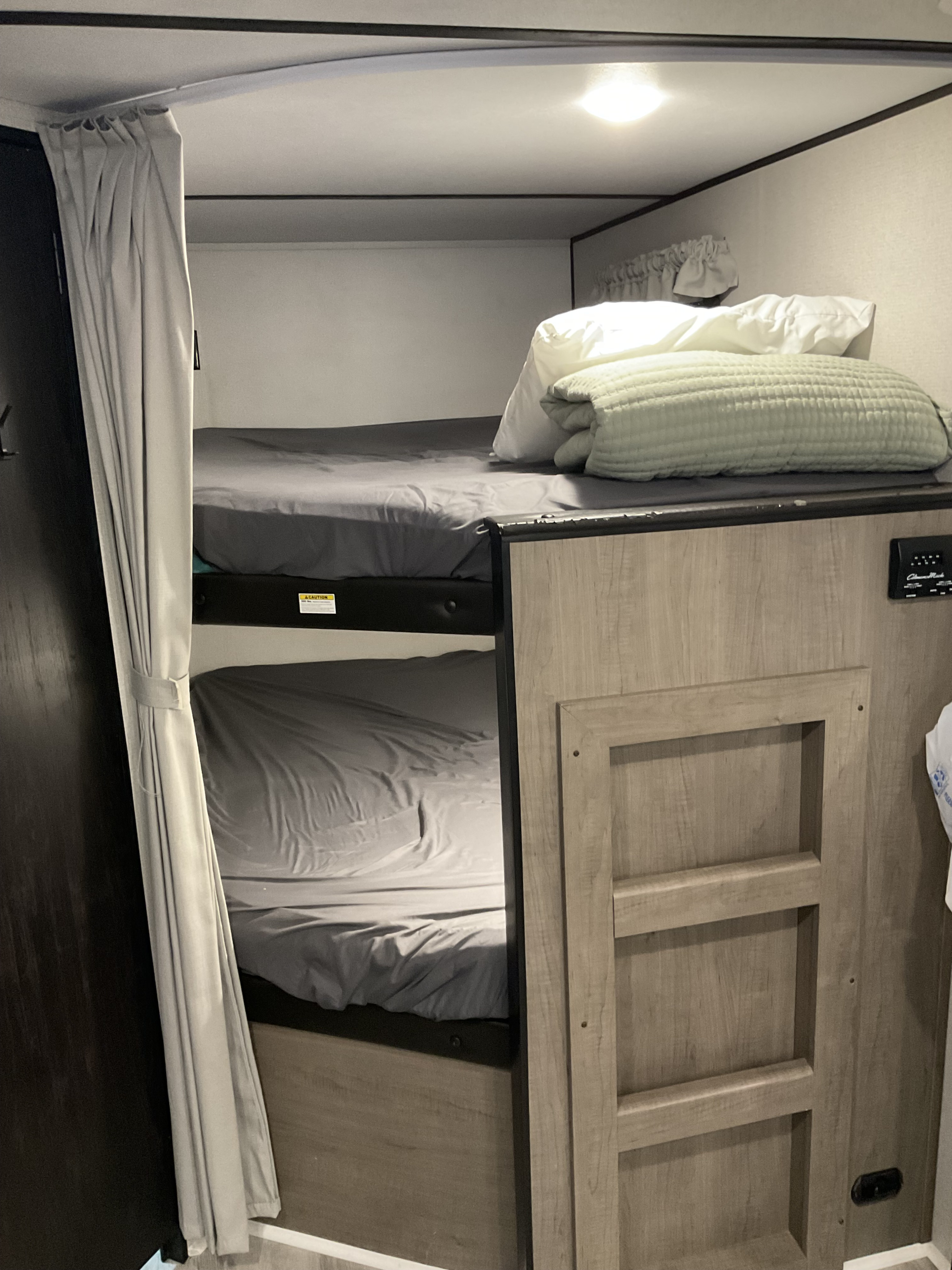 RV rental bunk beds: Two comfortable bunks with gray sheets, a privacy curtain, and bright interior lighting.. Keystone RV Hideout 2021