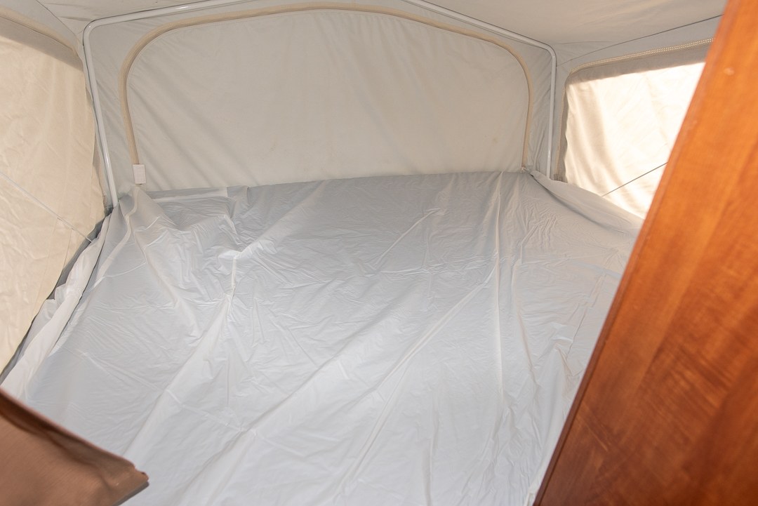 RV rental pop-up camper interior with a bed area covered by a crinkled white protective sheet. Light comes from a window.. Jayco Jay Feather Ultra Lite 2013