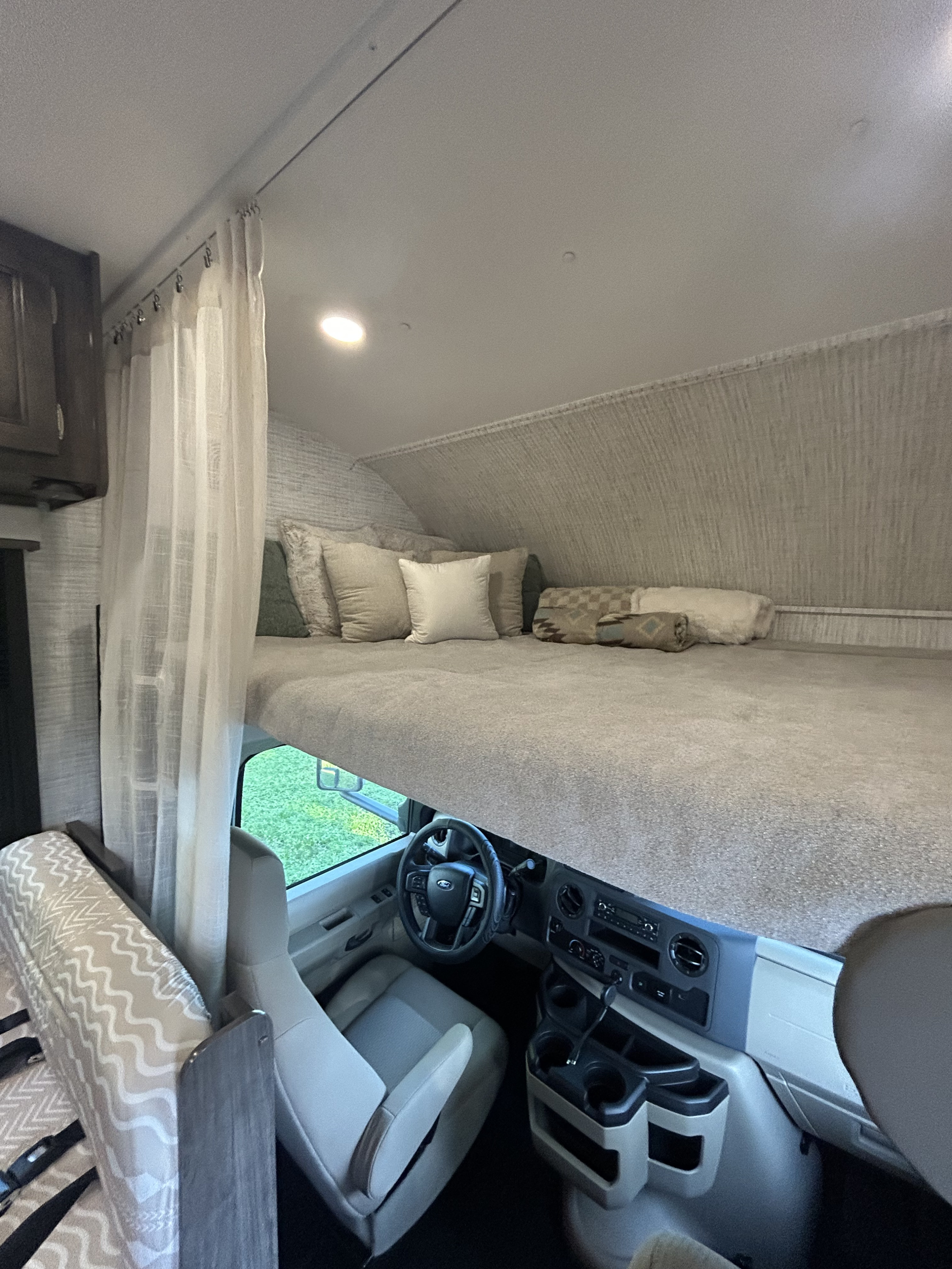 Overhead bunk bed with pillows in an RV rental, positioned above the vehicle's driver cabin and dashboard.. Entegra Ford Transit 2025