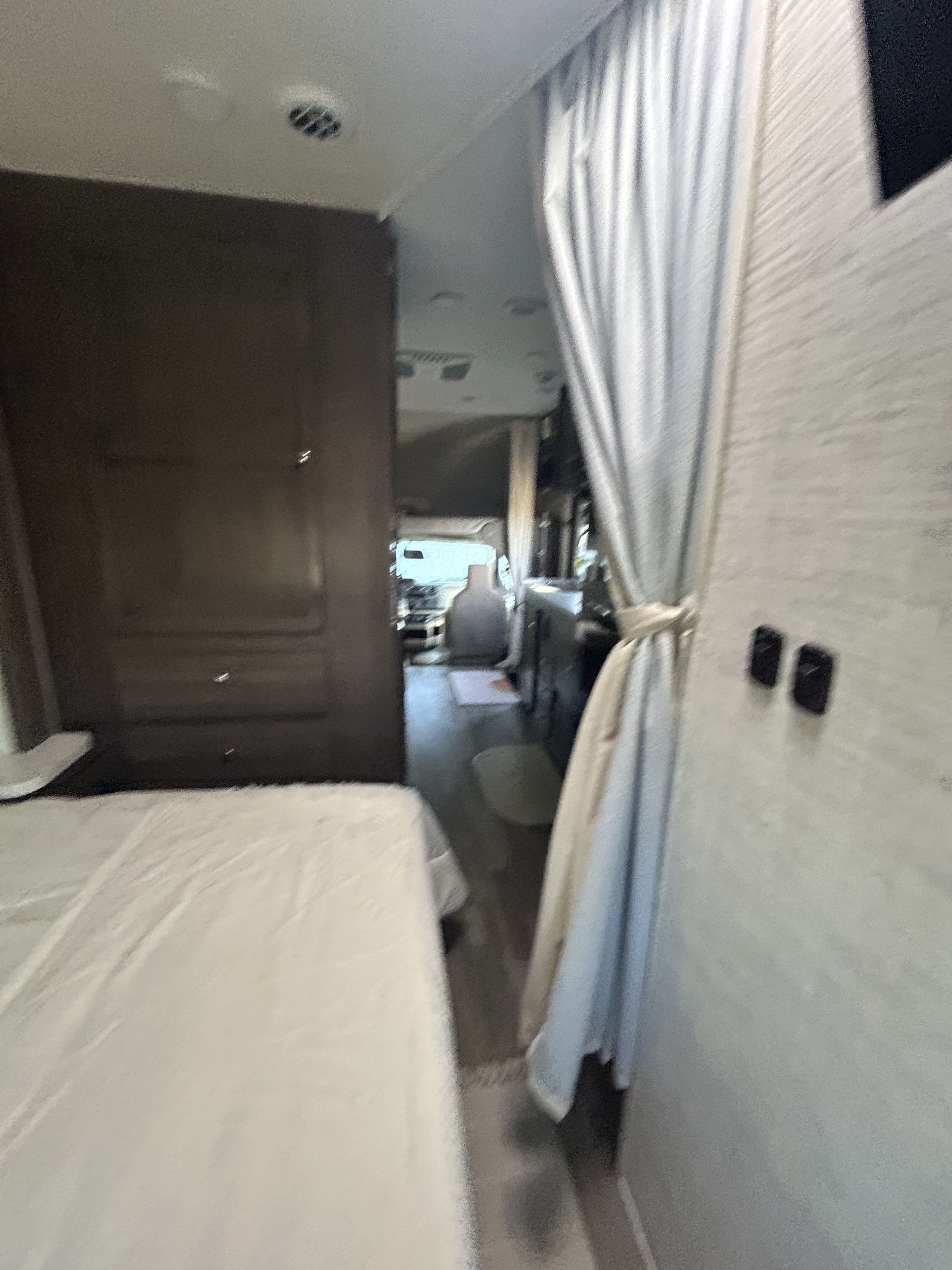 RV rental interior: bedroom with white bedding in foreground, dark storage on left, leading to front cabin.. Entegra Ford Transit 2025