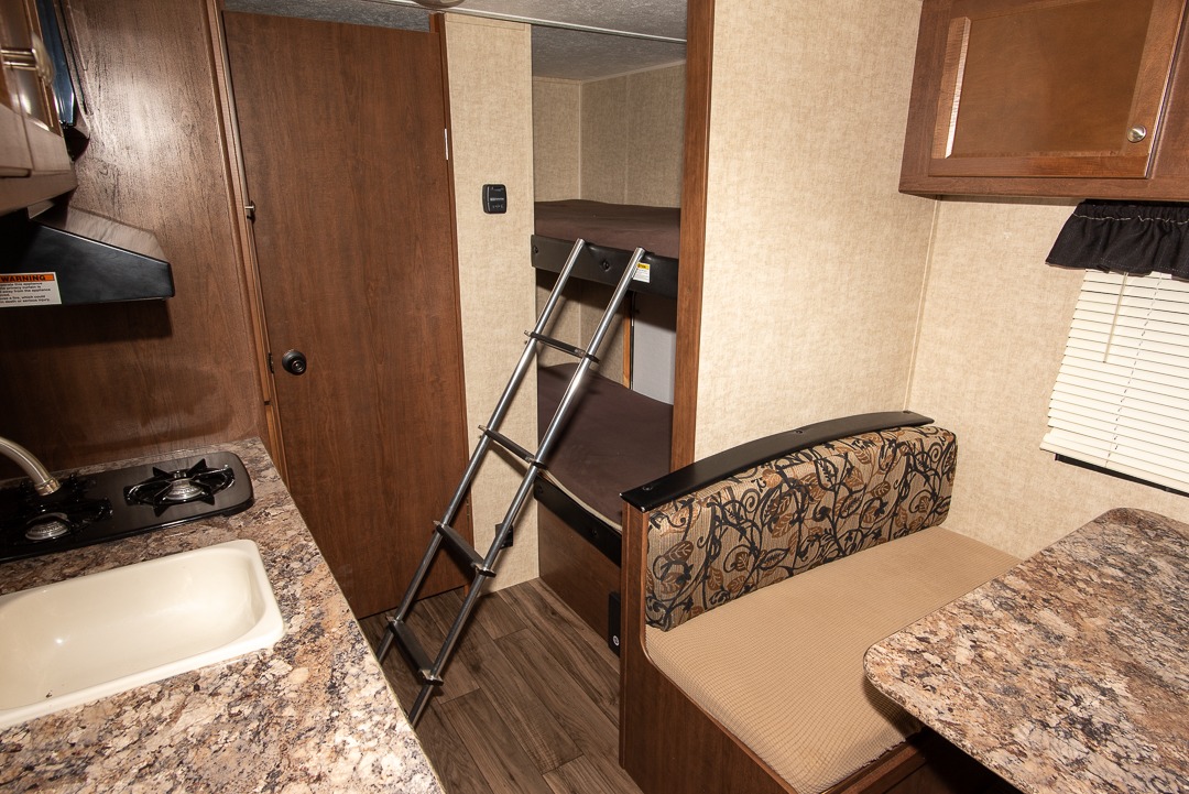 Cozy RV rental interior with a kitchen, bunk beds, and dinette area, offering comfort for your travels.. Keystone RV Hideout LHS Mini 2017